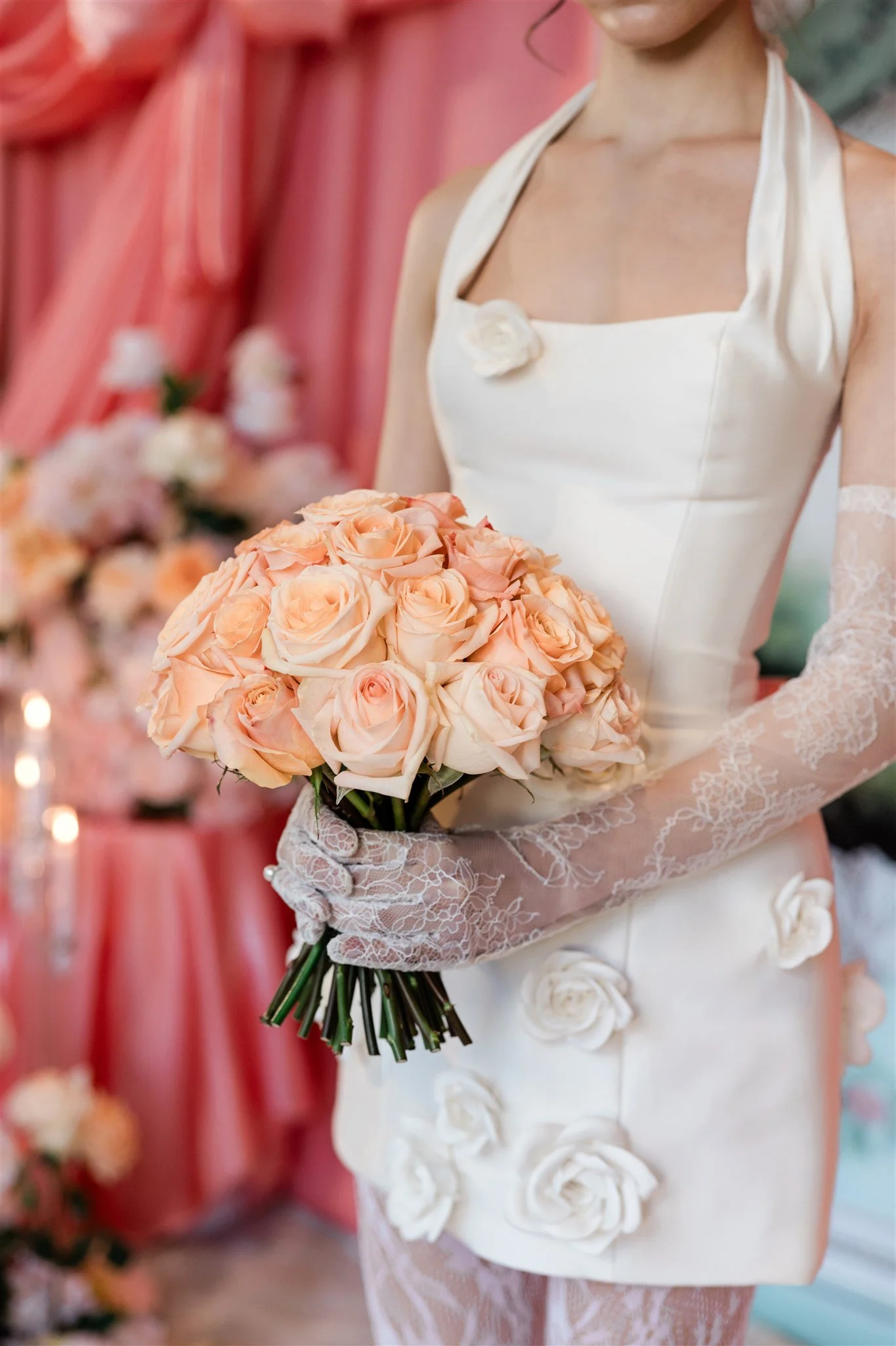 A woman in a white dress with lace sleeves holding a bouquet of peach-colored roses at a wedding or event.