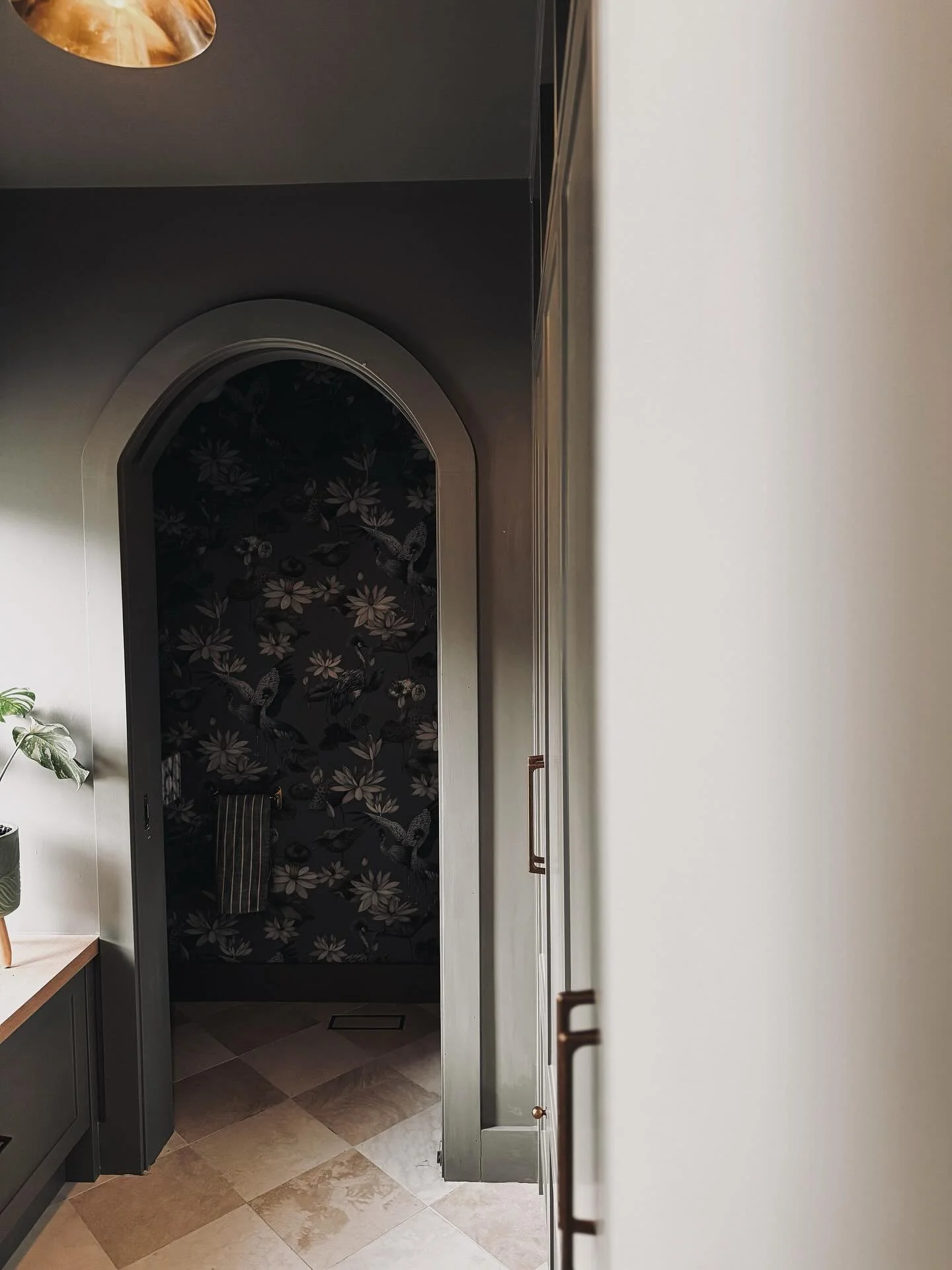 Step through the archway and into another world.
This powder room was designed to prove one thing: small spaces can tell the biggest stories.

From the veined marble sink to the moody, illustrated wallpaper and glowing brass details&mdash;every eleme