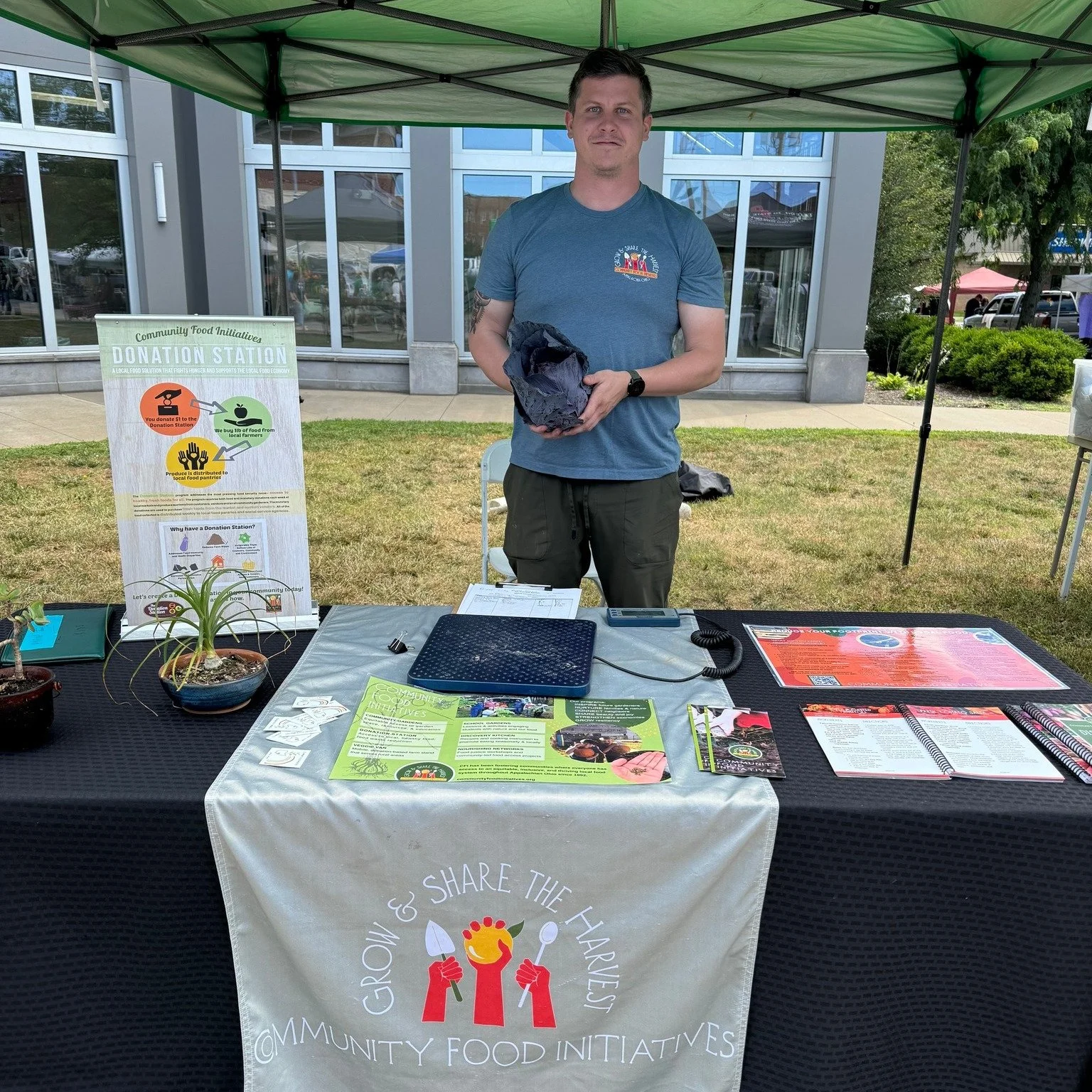 a young man standing behind a table with signage about the Donation Station