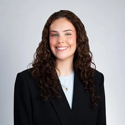 Smiling person with long wavy hair, wearing a red top and cream cardigan, arms crossed.