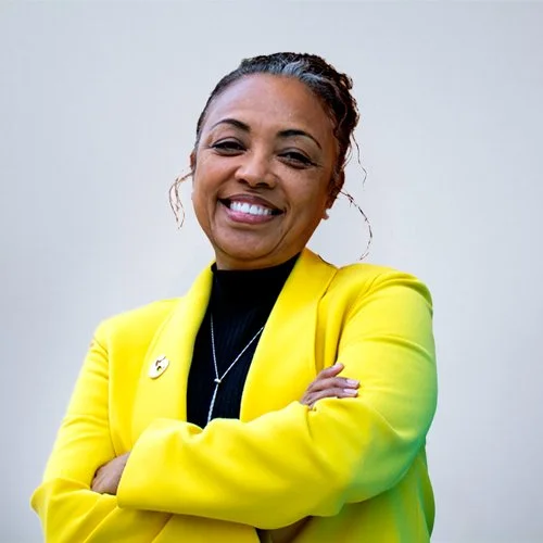 Smiling woman wearing a tan sweater and a light blue scarf against a gray background