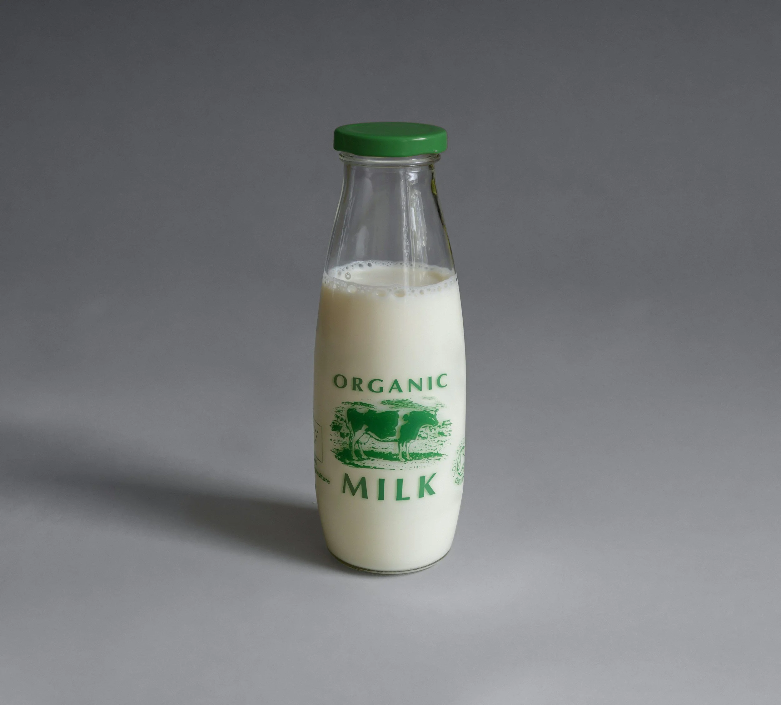 A glass bottle of organic milk with a green cap and label, placed on a gray surface with a gray background.