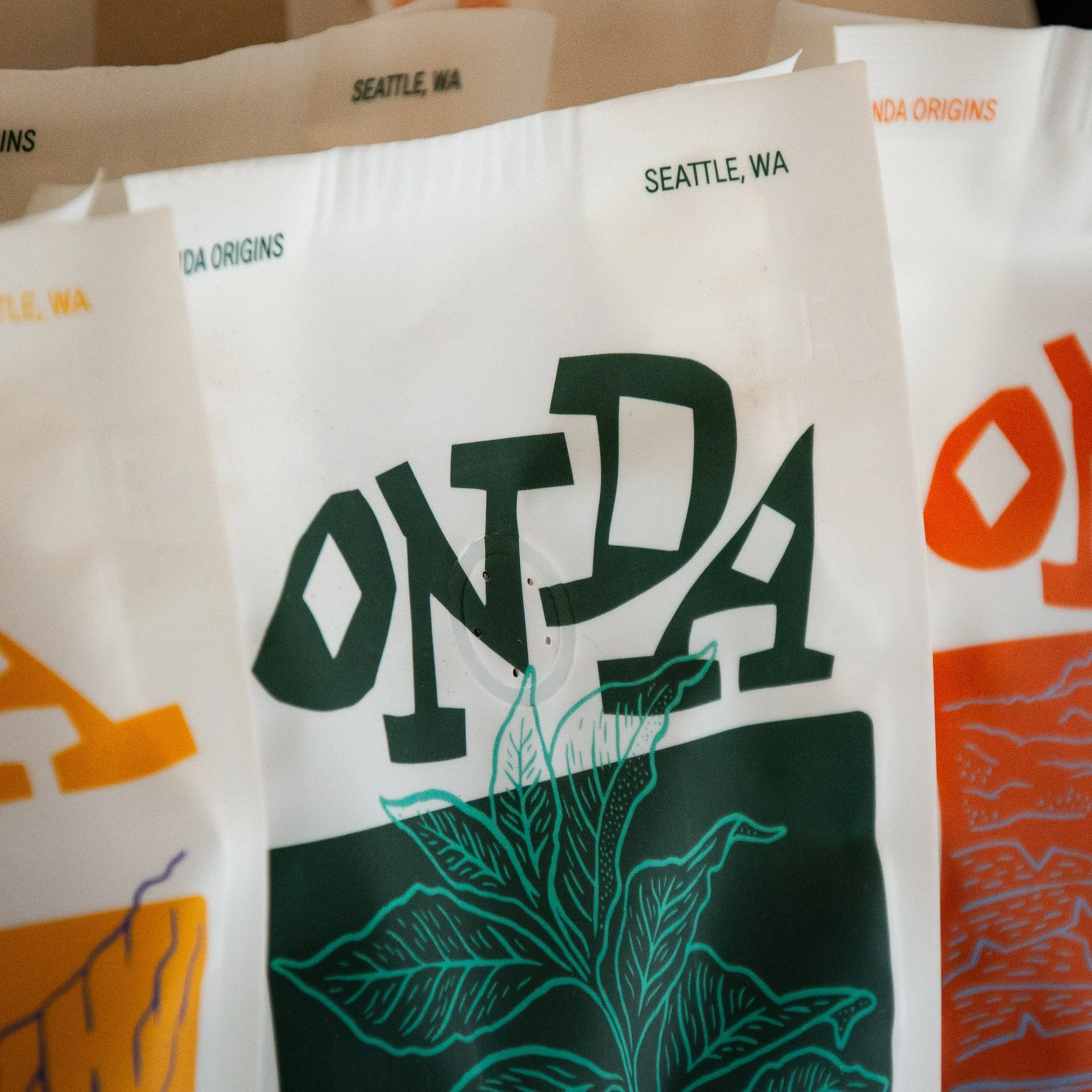 Bags of coffee from a brand called 'ONTDA', featuring a large illustration of a coffee plant with leaves, with the location 'Seattle, WA' printed on them.