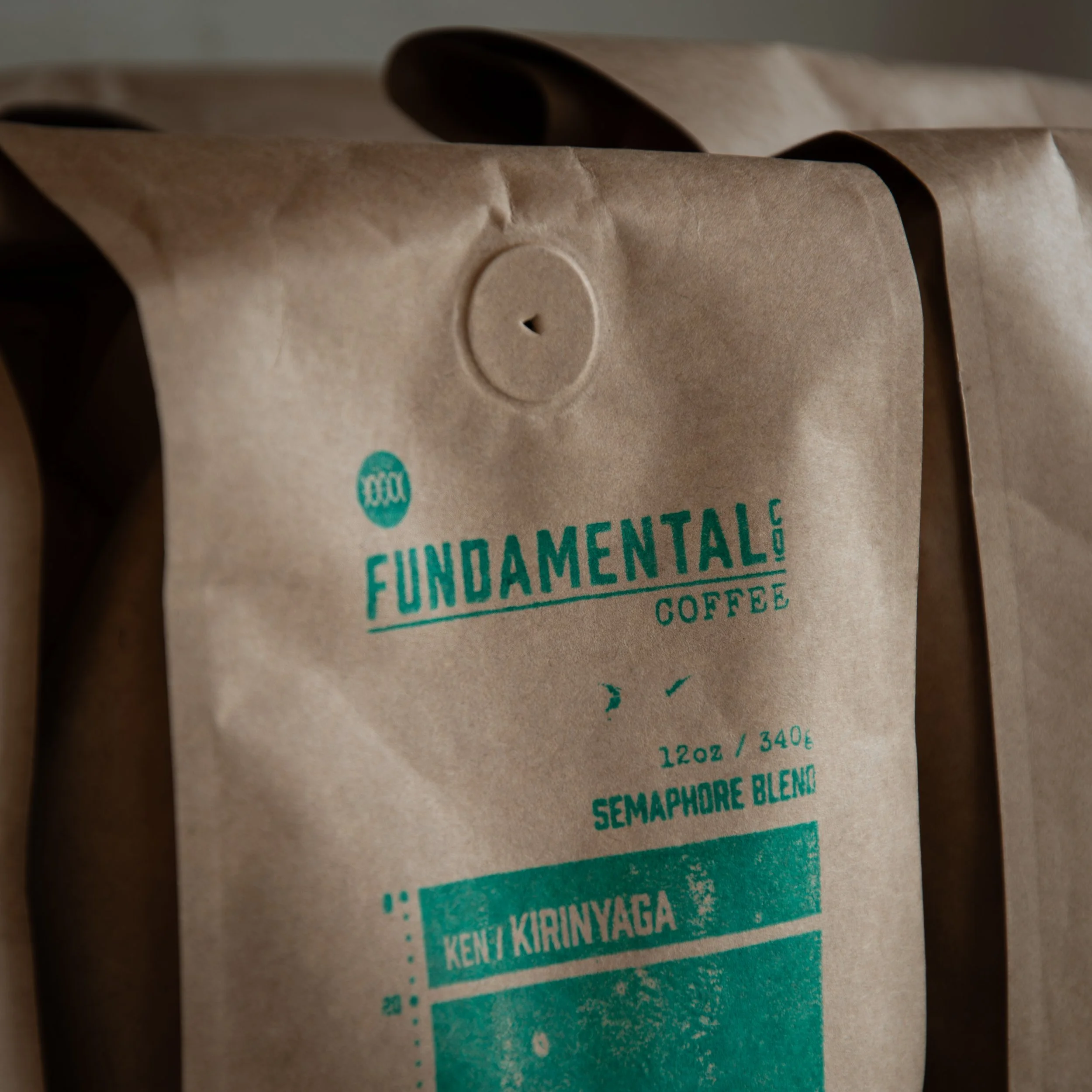Close-up of a brown paper coffee bag with green text and logo from Fundamental Coffee, labeled as Semaphore Blend with Ken/Kirinayaga origin, 12 oz.