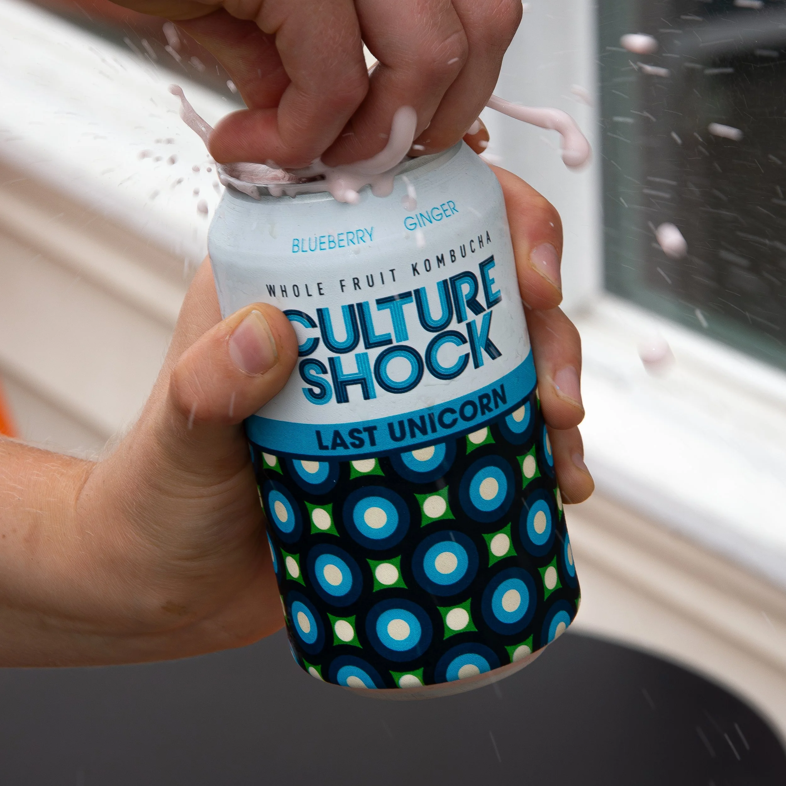 Person opening a can of Culture Shock Last Unicorn flavored kombucha, with pink foam spilling out as the can is opened.