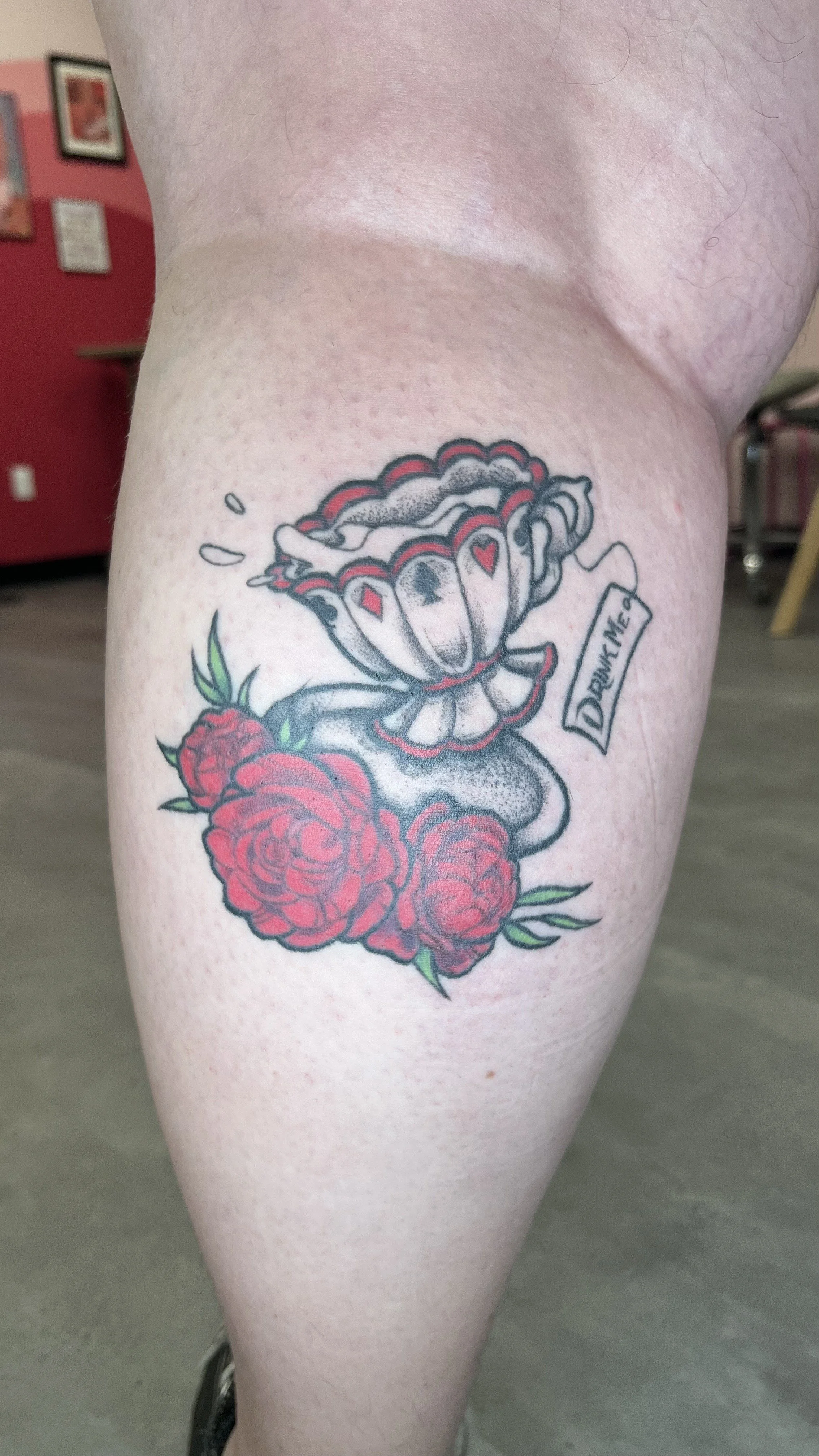 Tattoo of a rose and a scroll with the text 'DRINK ME' on a person's thigh.