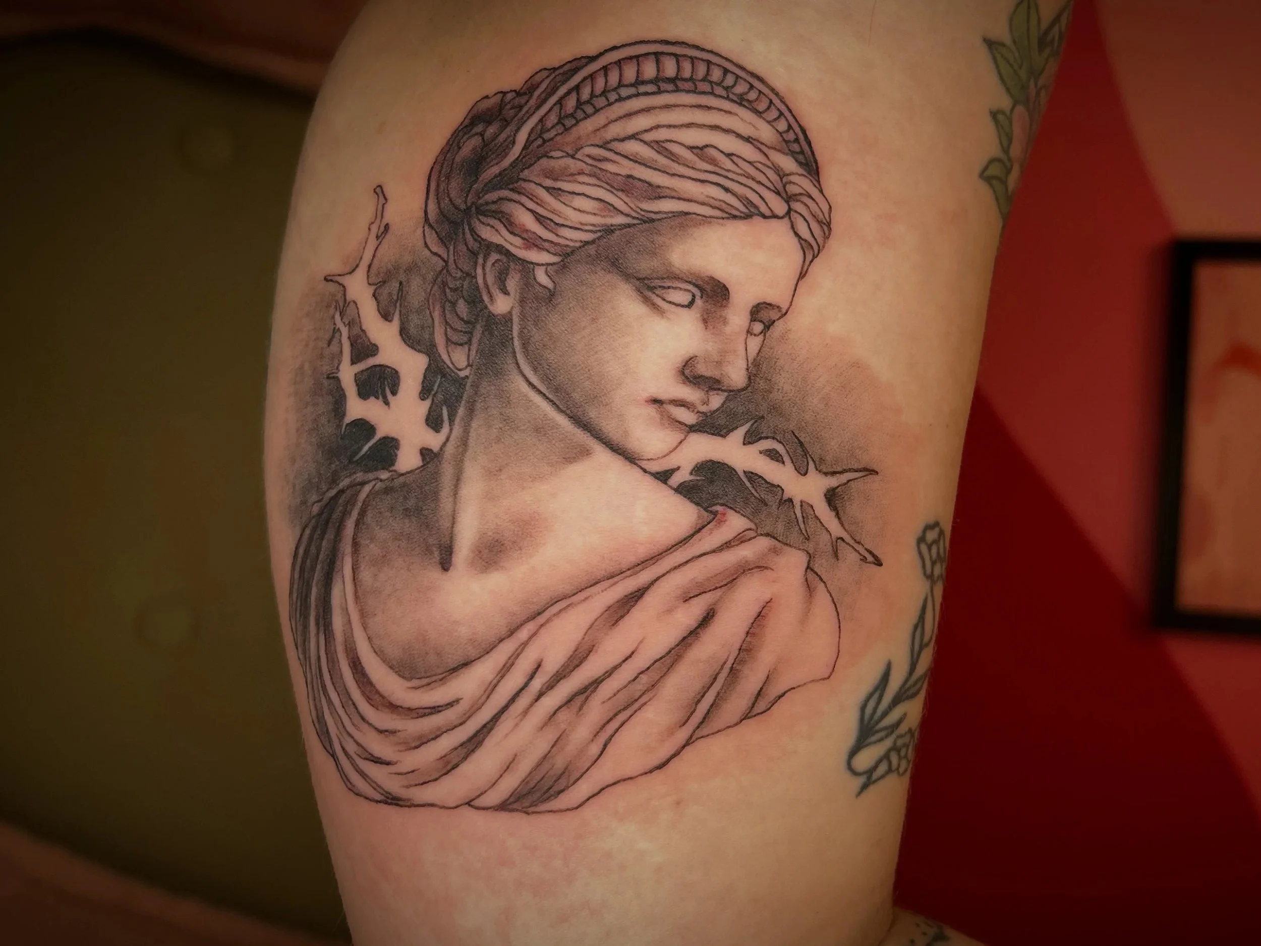 Black and gray tattoo of a woman's face with braided hair, surrounded by swirling lines and abstract shapes on skin.