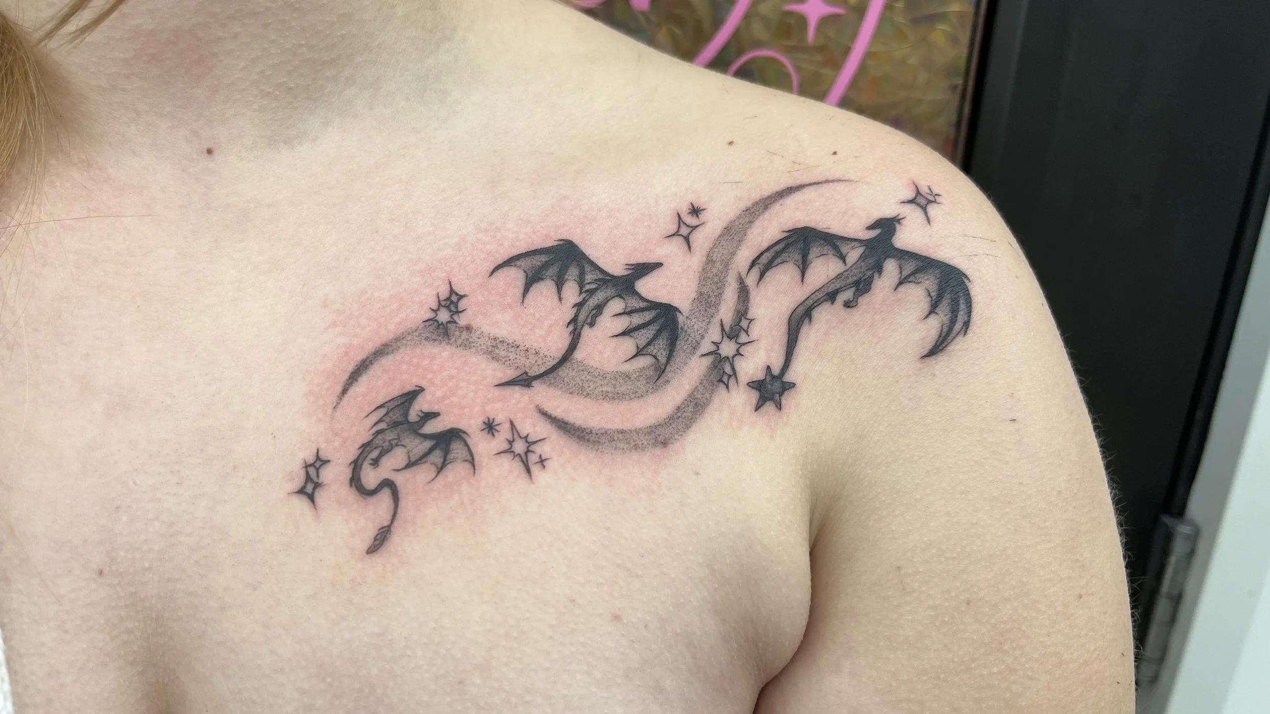Tattoo of a small dragon with wings and stars along the shoulder.