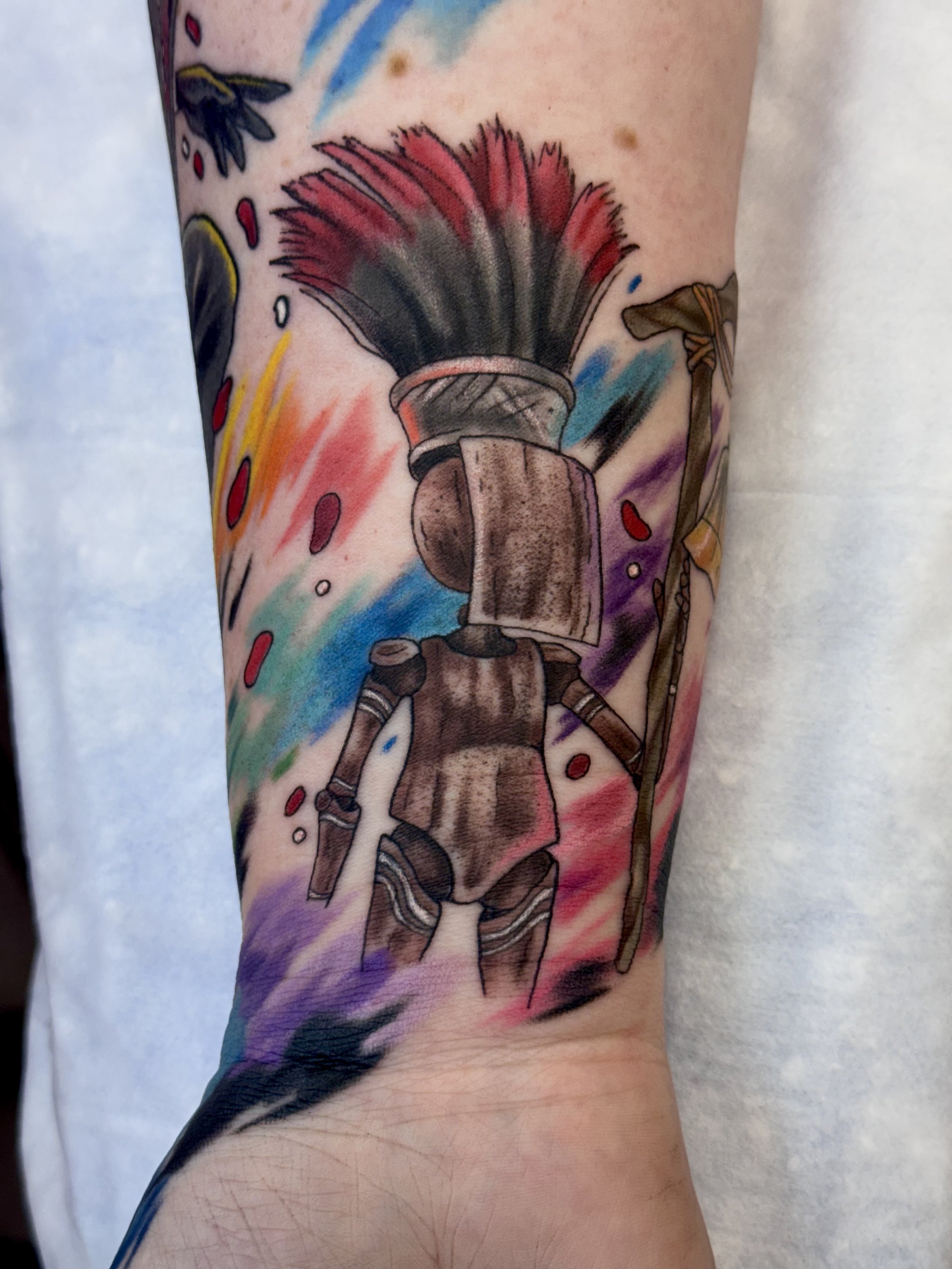 Colorful tattoo of a person in a medieval knight costume carrying a large, colorful feathered fan on a person's arm.
