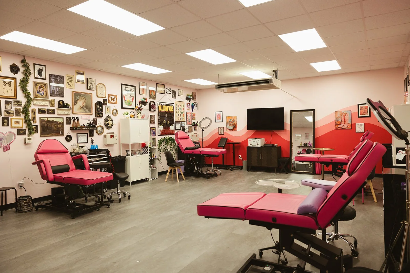 Interior of a tattoo studio with pink recliner chairs, an art gallery wall, and tattoo equipment.