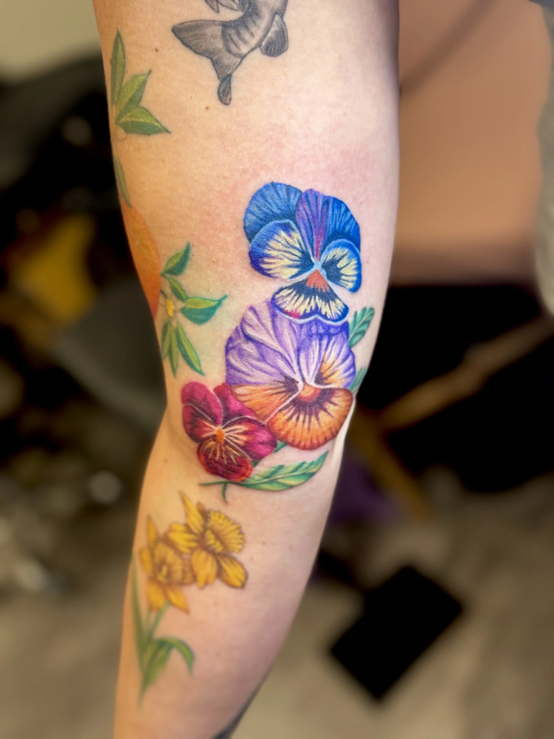 Close-up of a person's arm with a colorful tattoo of flowers and a butterfly.