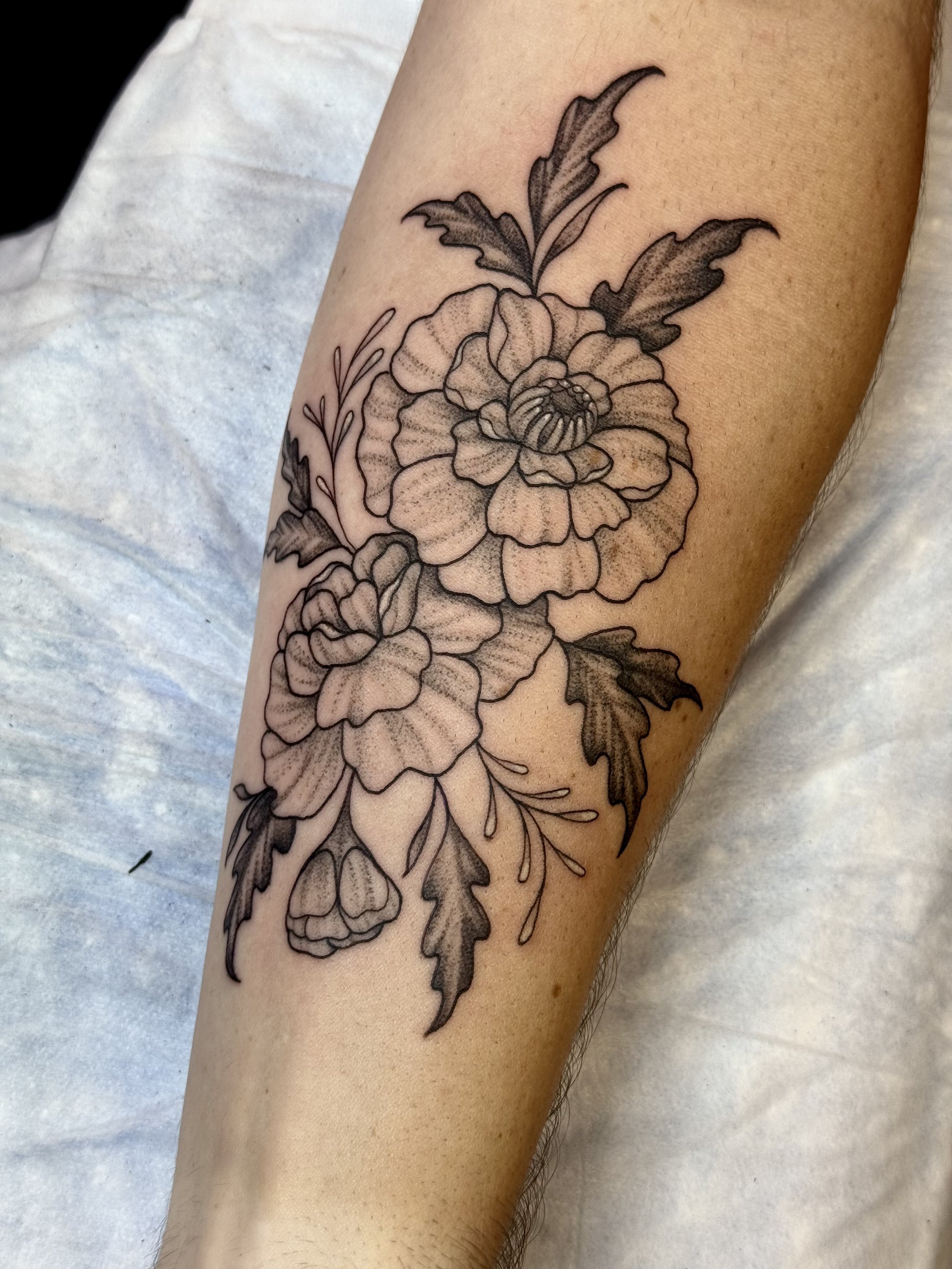 Black and grey floral tattoo on person's forearm featuring a large flower with detailed petals and leaves.