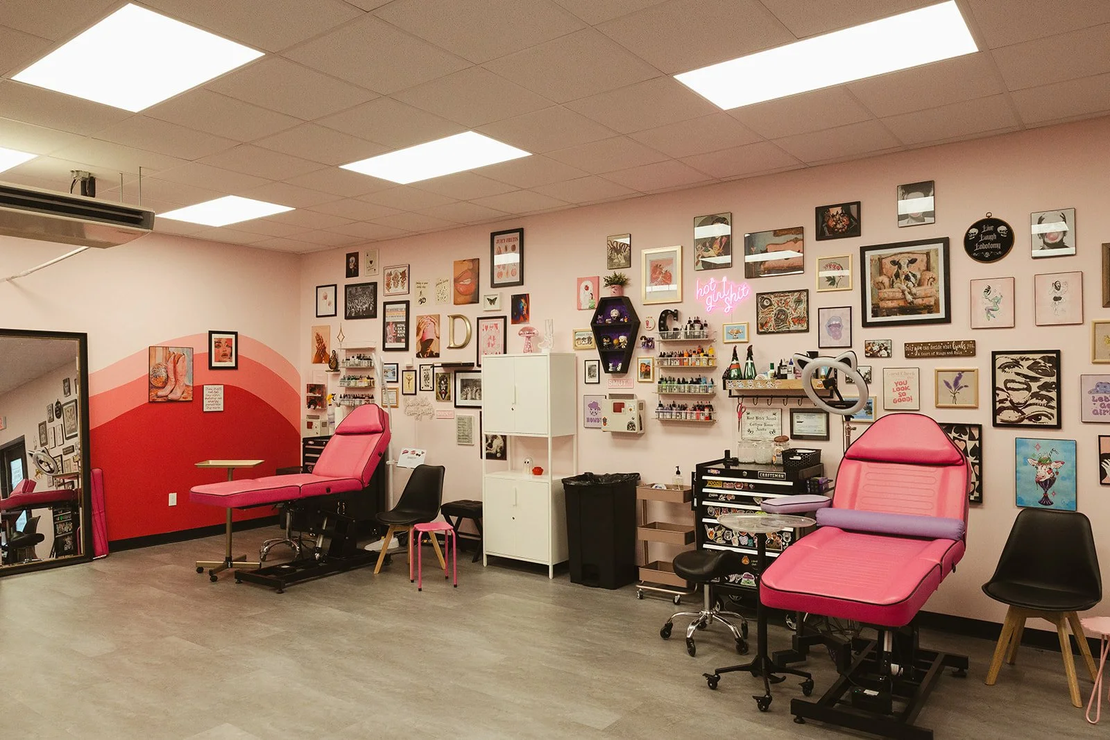 A room with pink tattoo chairs, wall art, and tattoo supplies, suggesting a tattoo or beauty studio.