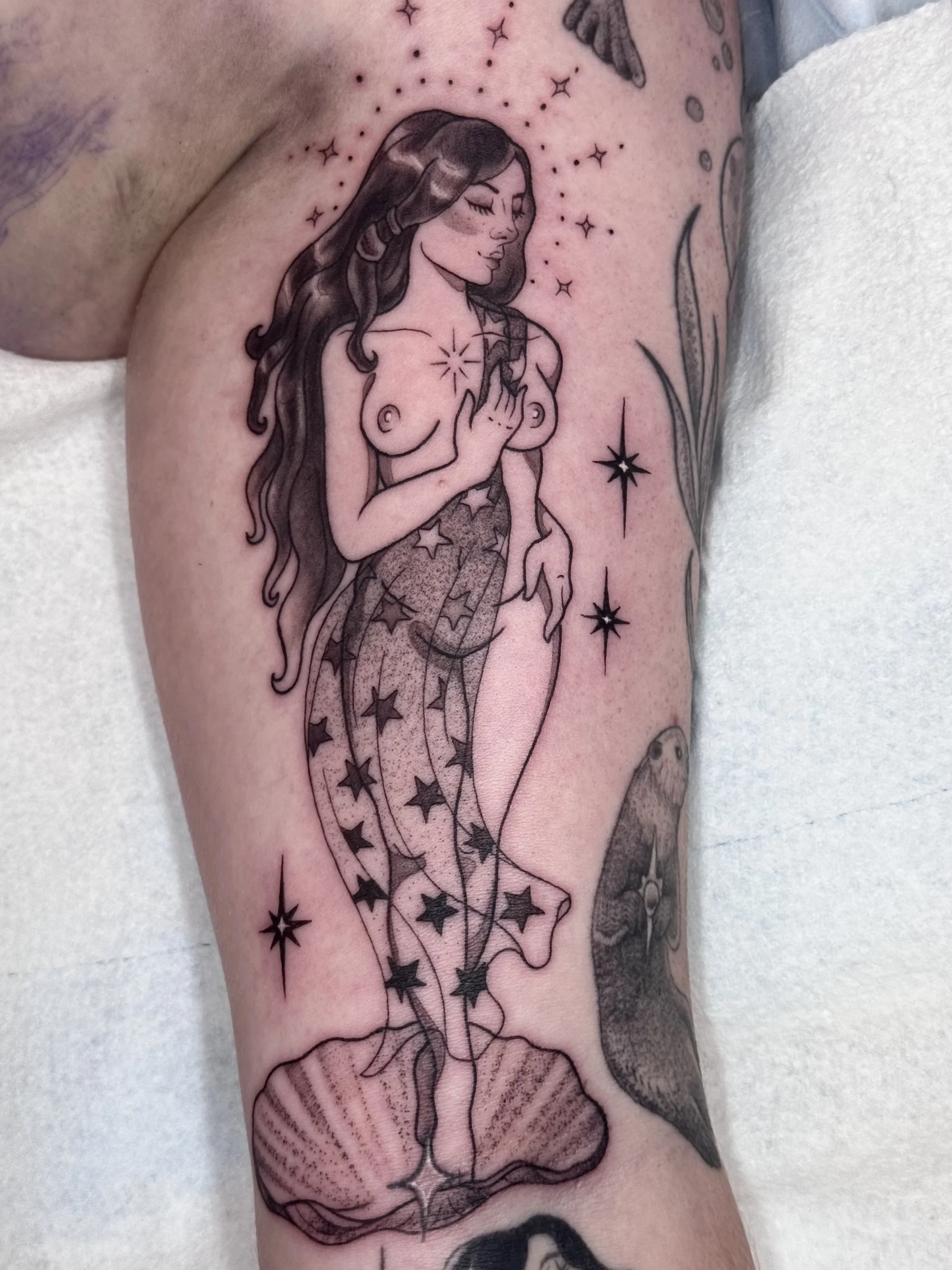 Tattoo of a woman with long hair, closed eyes, and hand on her chest, surrounded by stars and celestial imagery.