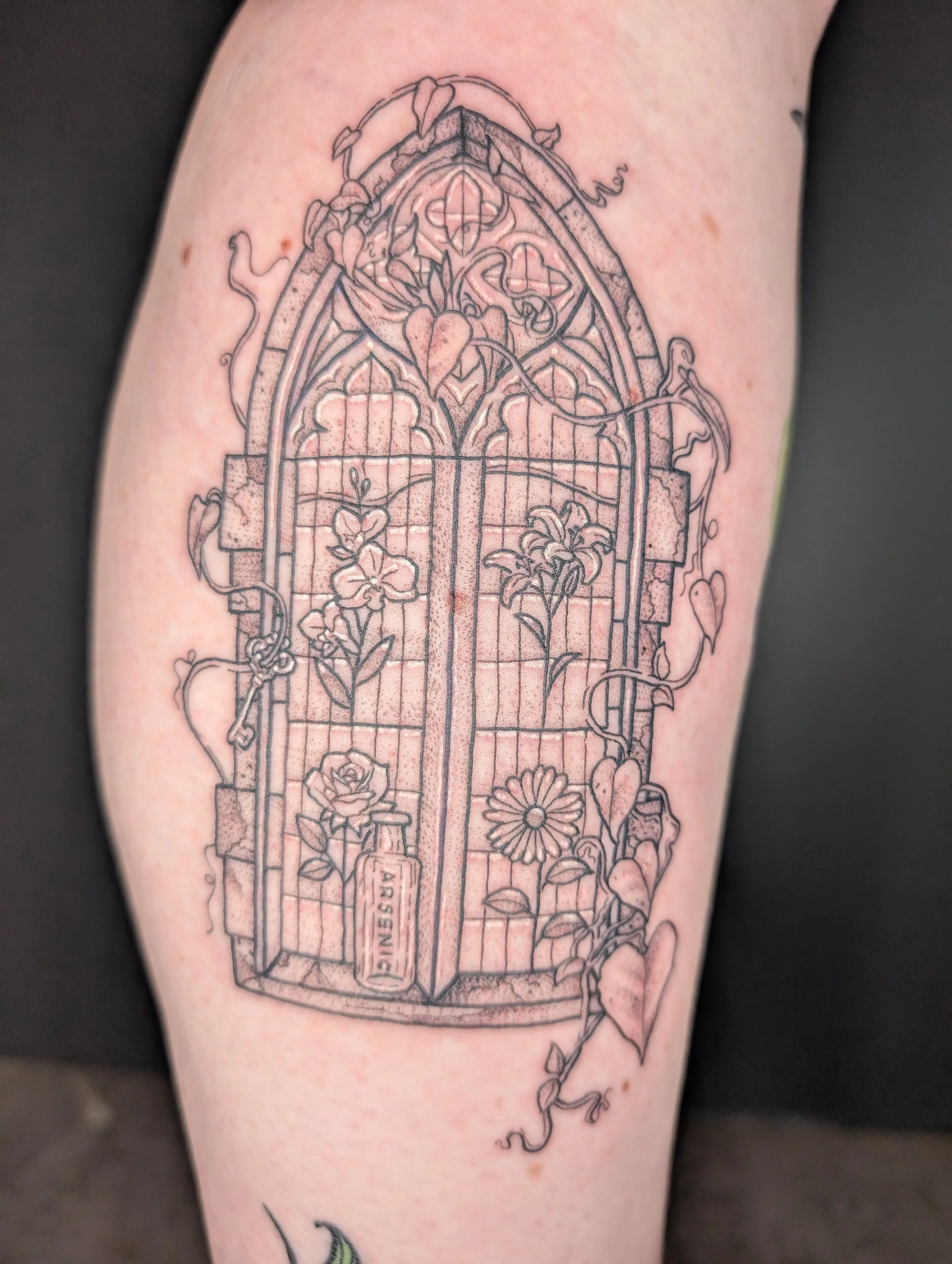 A tattoo of a stained glass window with flowers and vines on a person's upper arm.