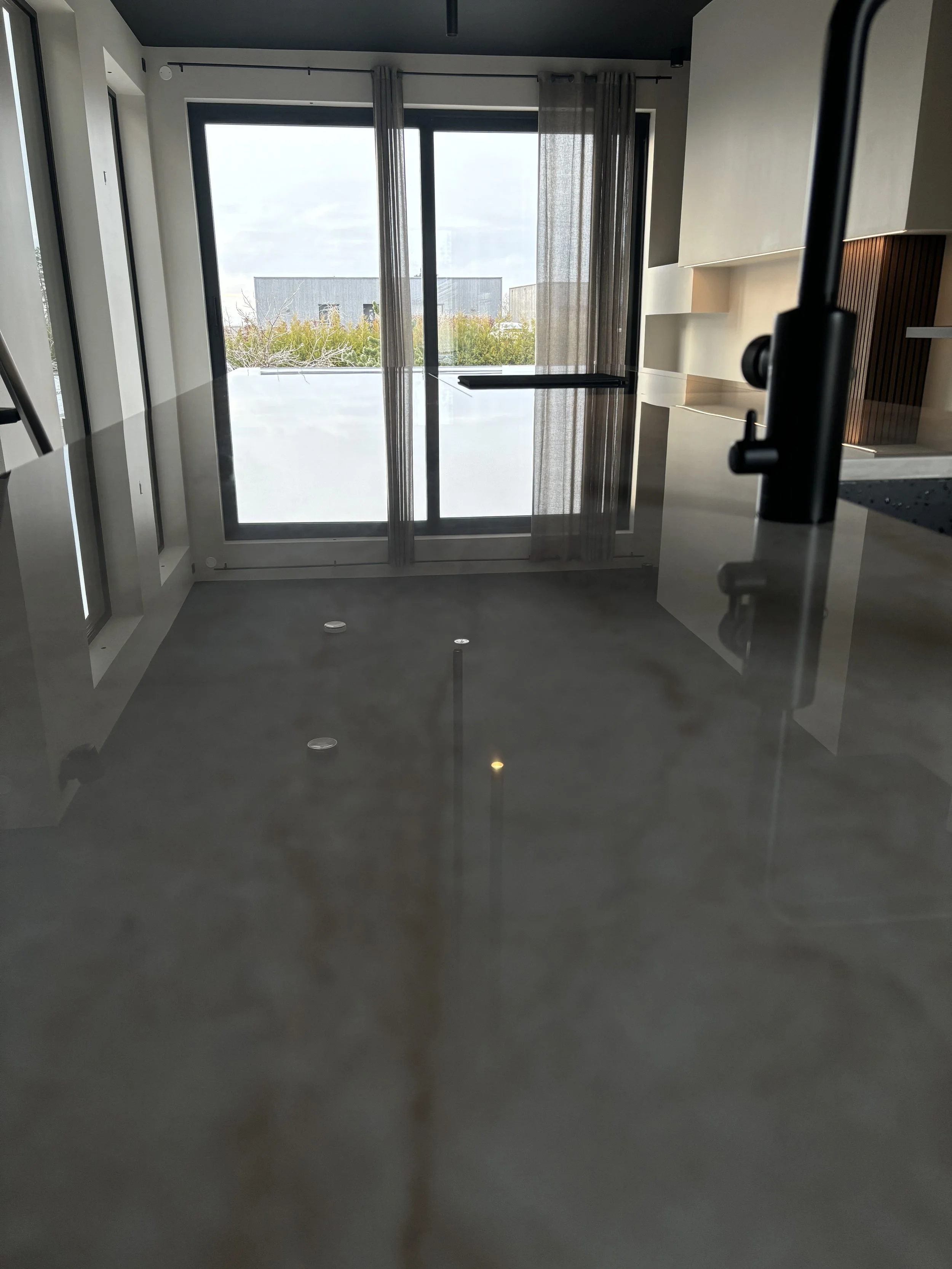 Interiör av ett modernt kök med stor glasdörr som leder utomhus, med gardiner och något som liknar ett köksbänk till höger.