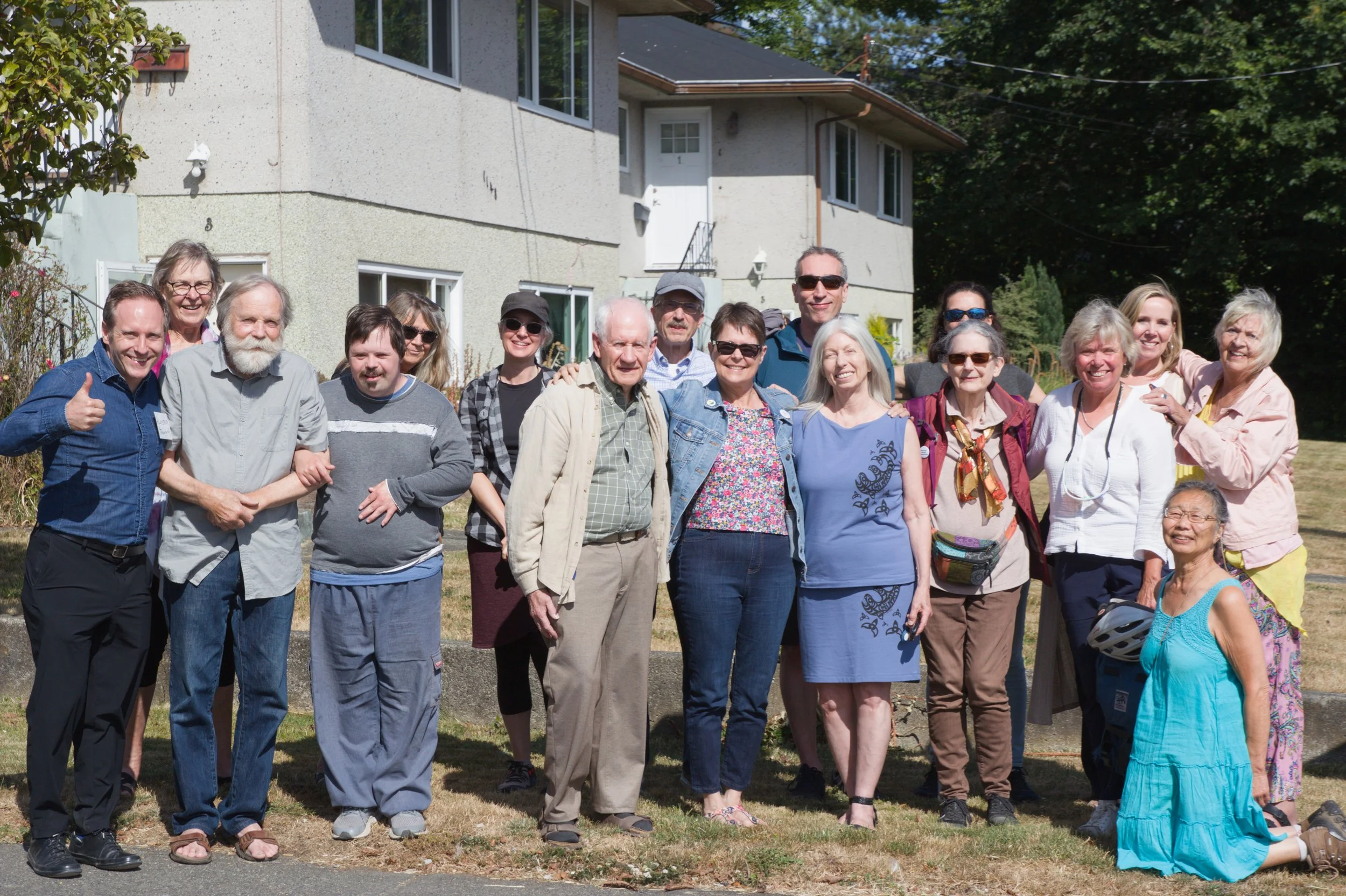 A group of diverse members of Esquimalt Village Cohousing standing in front of the future community site