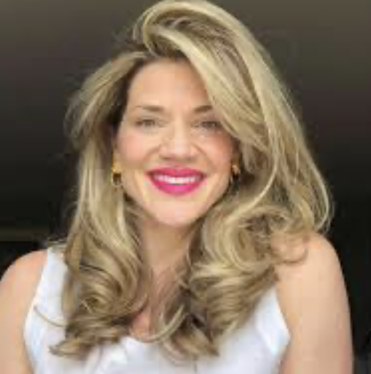Person with long, wavy blonde hair and bright lipstick smiling.