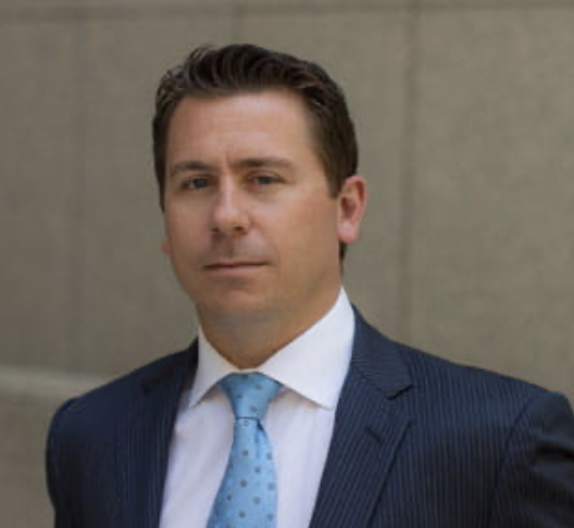 A person in a suit and tie standing in front of a stone wall.
