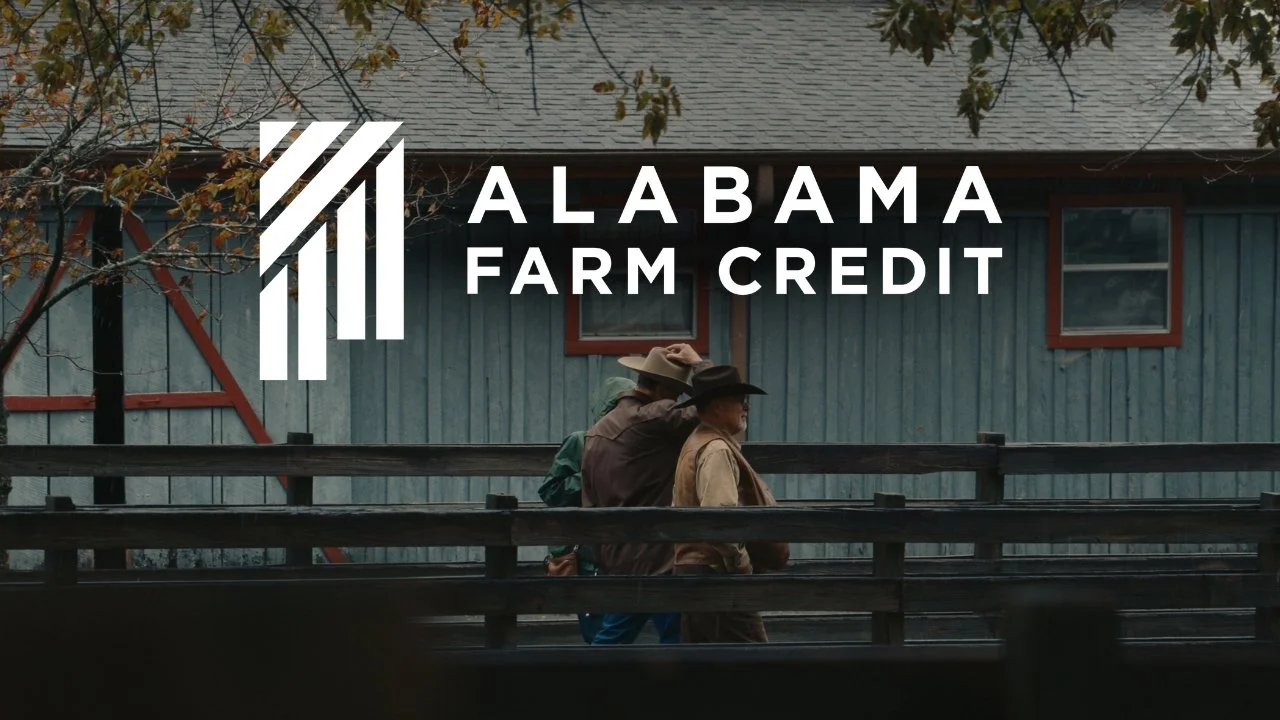 Three people dressed as cowboys walking on a wooden bridge in front of a blue barn with small windows, trees with autumn leaves overhead, with Alabama Farm Credit logo in the upper left corner.