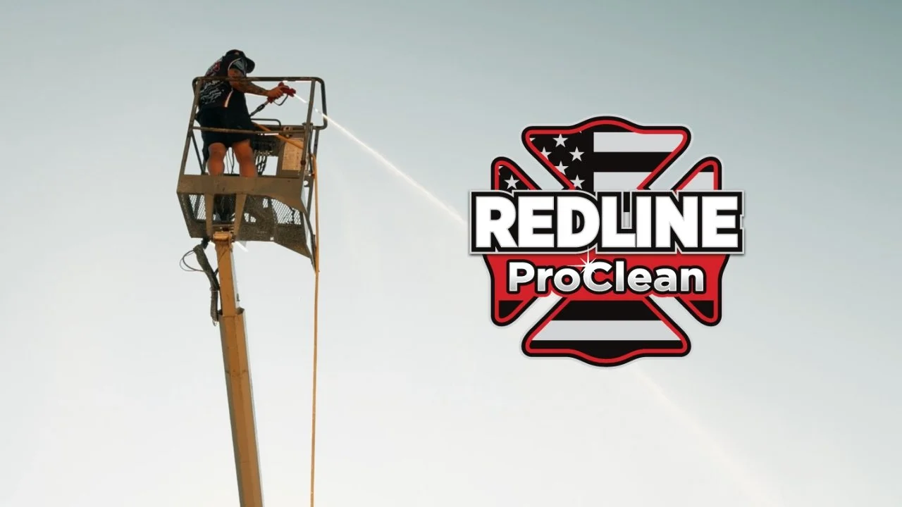 A worker on a lift cleaning an American flag logo with a spray hose.