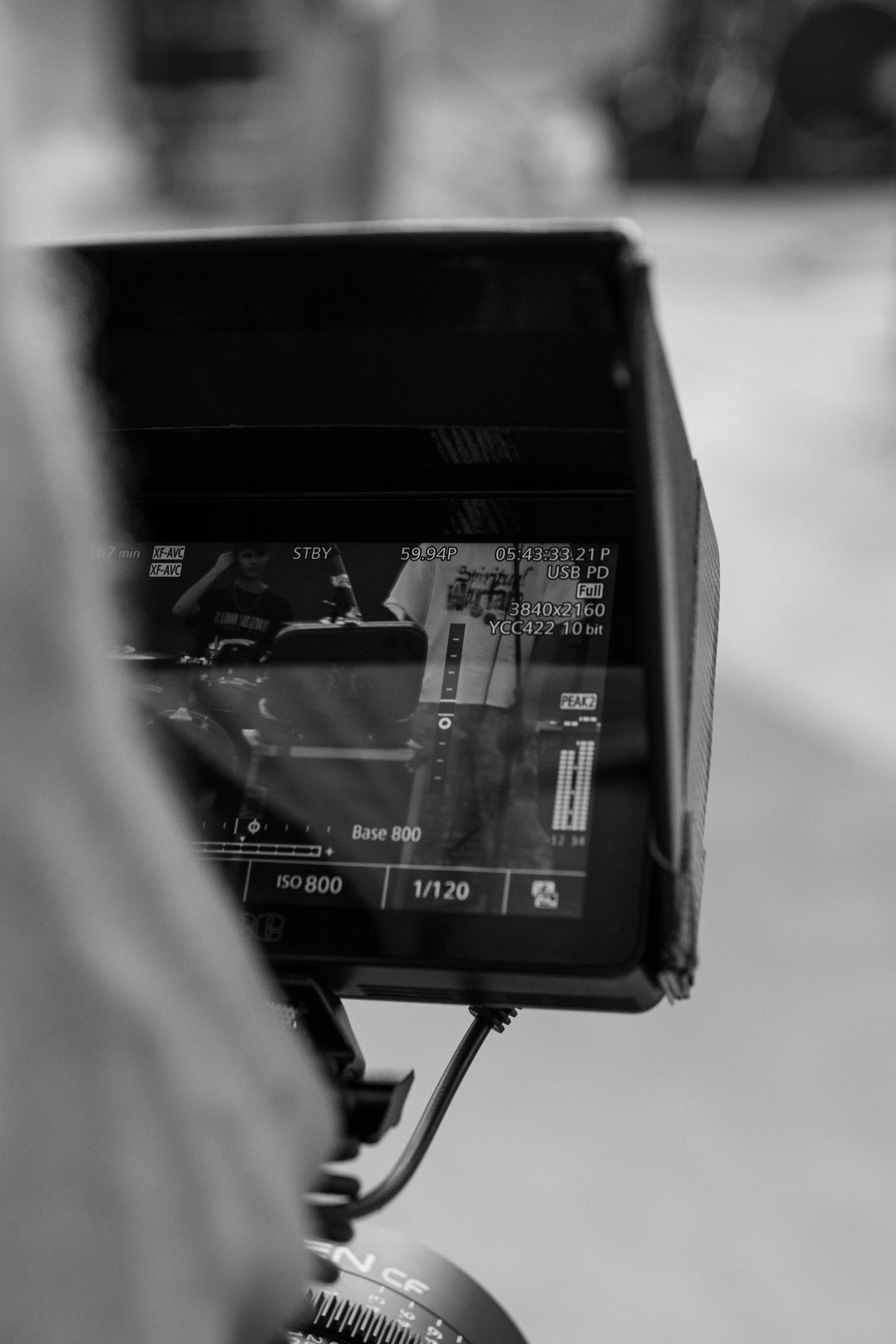 Black and white close-up of a camera screen displaying video footage, showing people in the background.