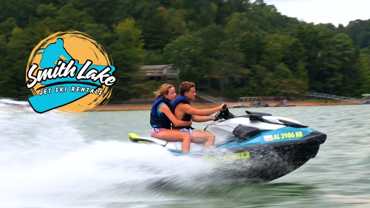 Two people riding a jet ski on a lake with trees in the background and a logo for Smith Lake Jet Ski Rentals in the top left corner.