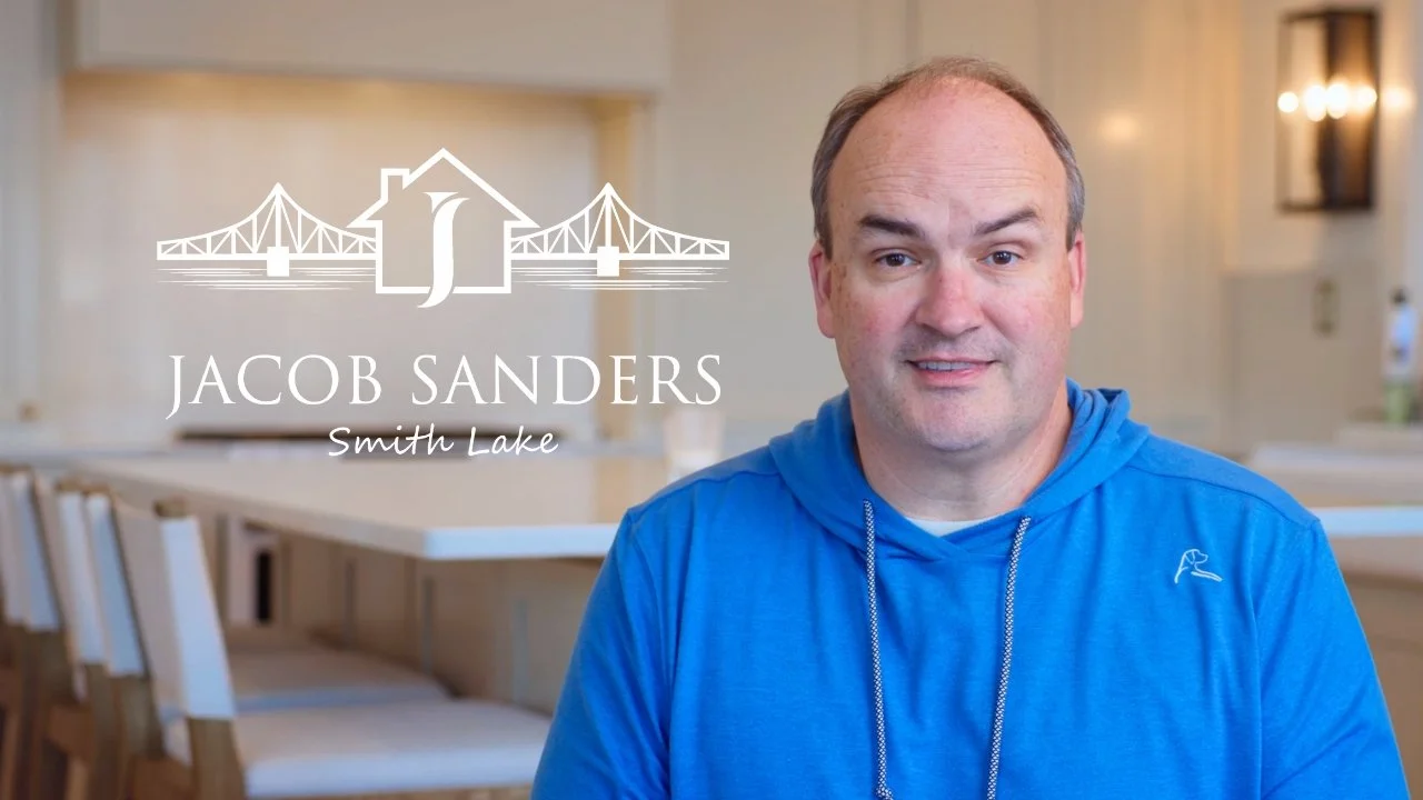 A man in a blue hoodie sitting at a table in a bright room with a logo overlay that says Jacob Sanders, Smith Lake, with a bridge and house graphic.