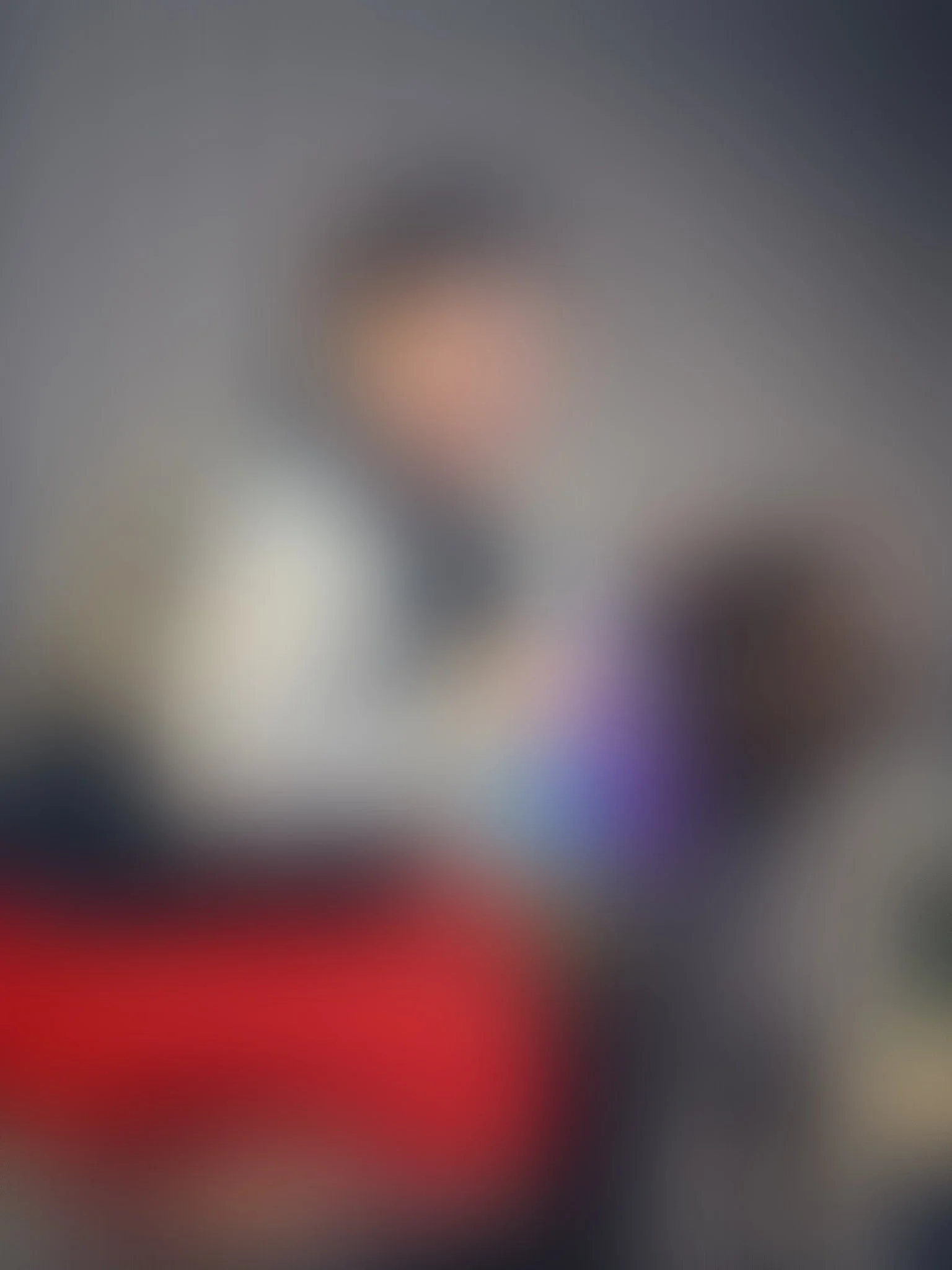 A person smiling, kneeling beside a dog while holding award ribbons. The dog has a shaggy coat and is sitting. They are outdoors, in front of a wooden wall.