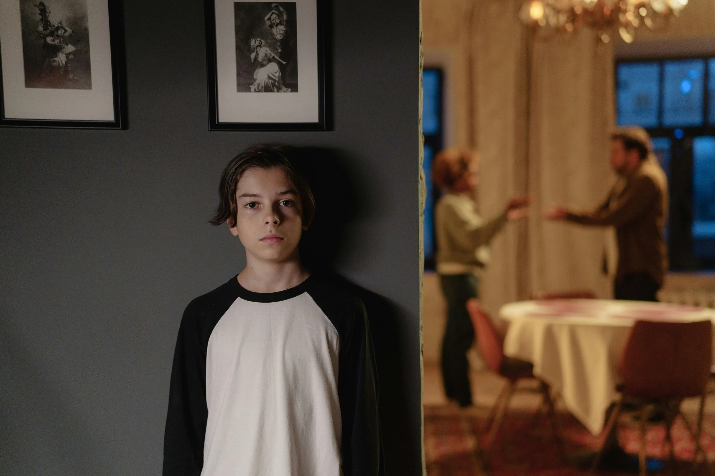 Pre-teen child standing alone taking a break from family New Year celebration in background, showing the importance of New Year anxious kids support through permission to step away when overwhelmed