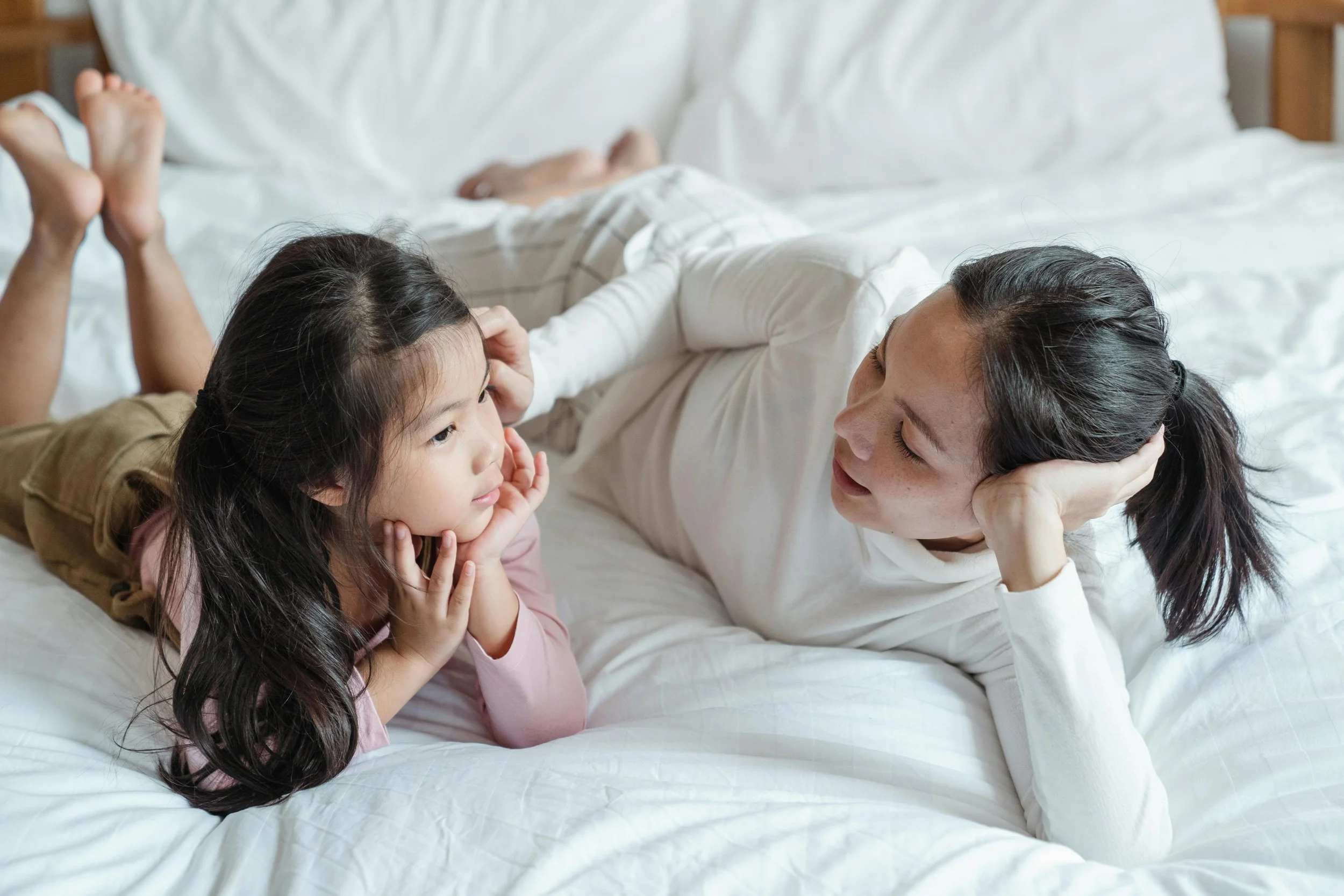 Mother and young daughter having peaceful conversation while lying on bed together, demonstrating connection and emotional support for managing kids emotions during celebrations through calm parent-child interactions
