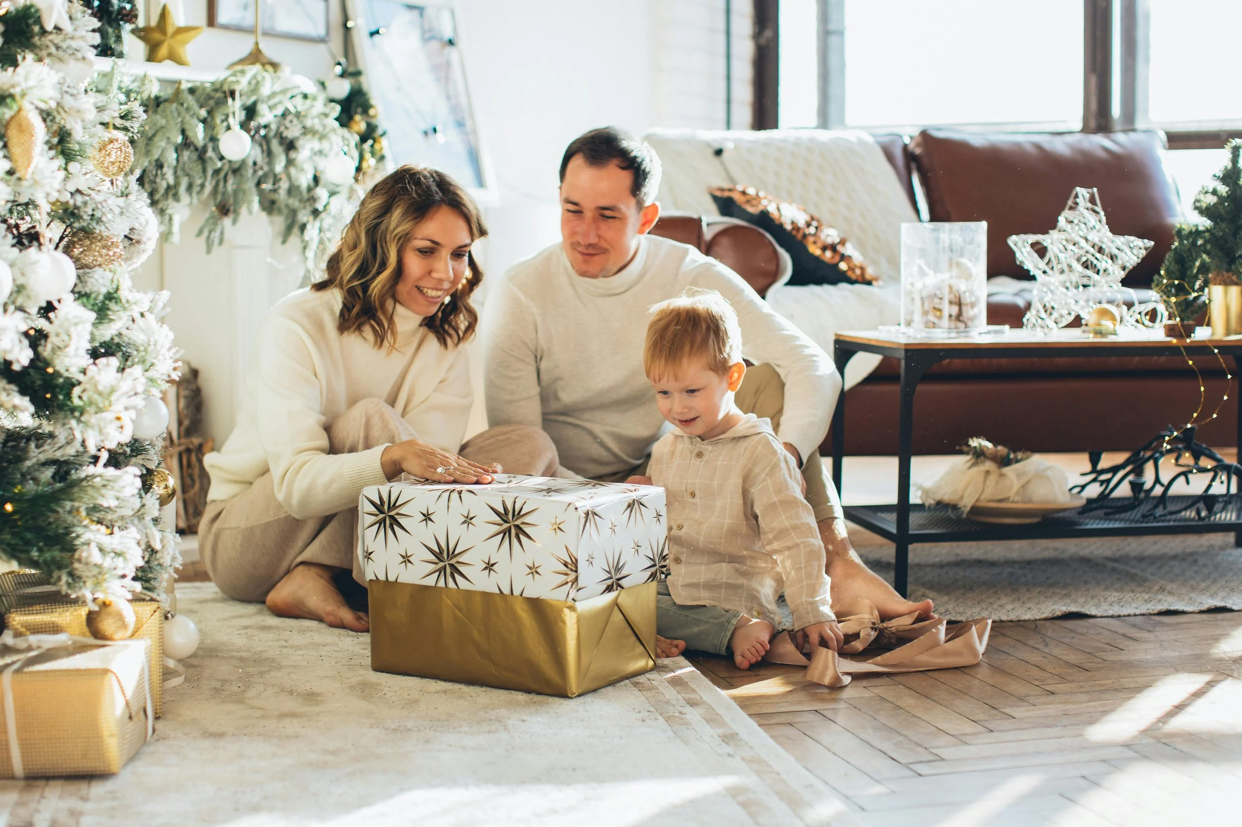 Mother, father, and young son embracing warmly near decorated Christmas tree, illustrating how managing holiday stress children involves creating connection through calm, meaningful moments together