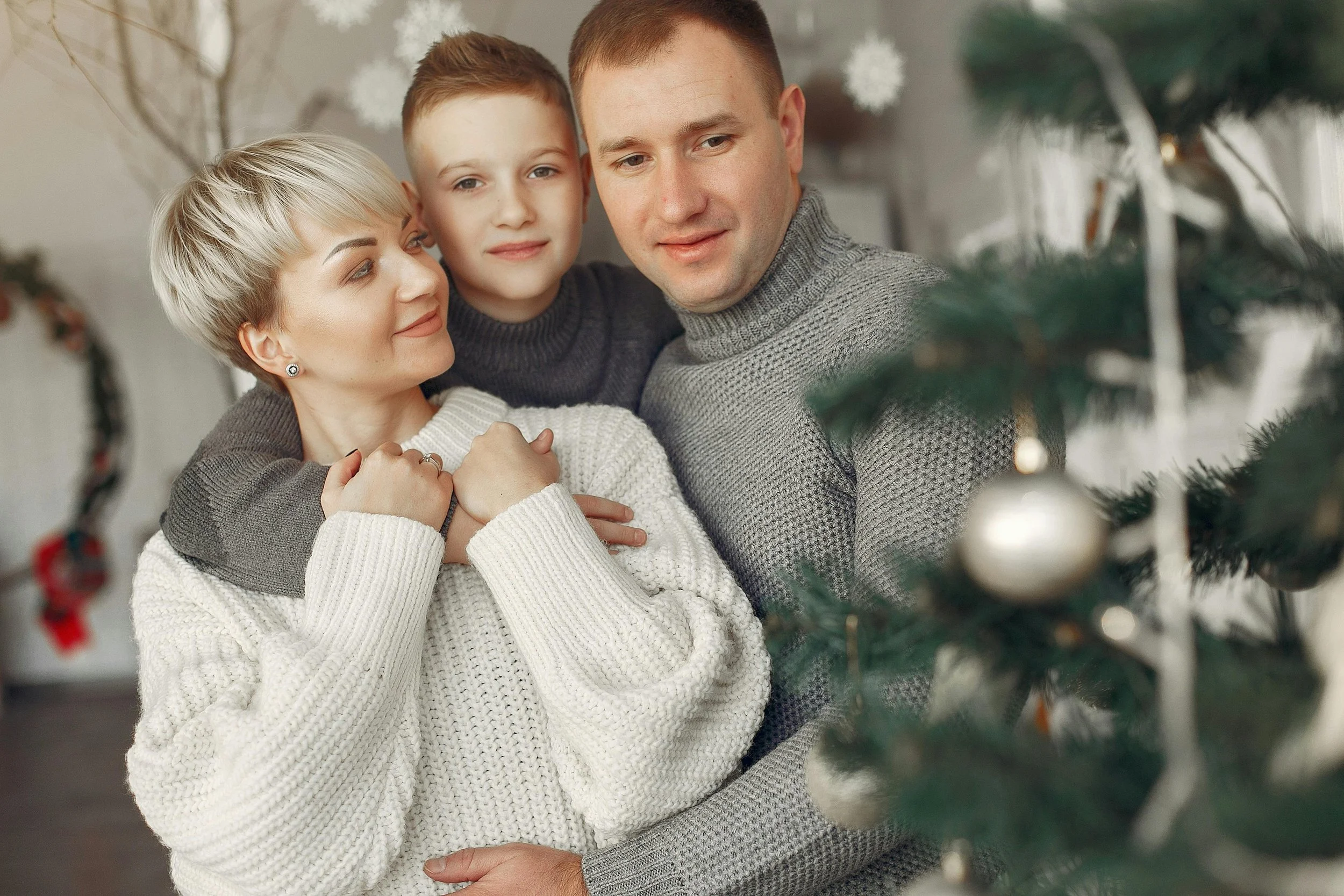Parents and young child joyfully opening wrapped holiday gifts by decorated Christmas tree, demonstrating strategies for reducing holiday stress children through meaningful family moments and simple traditions