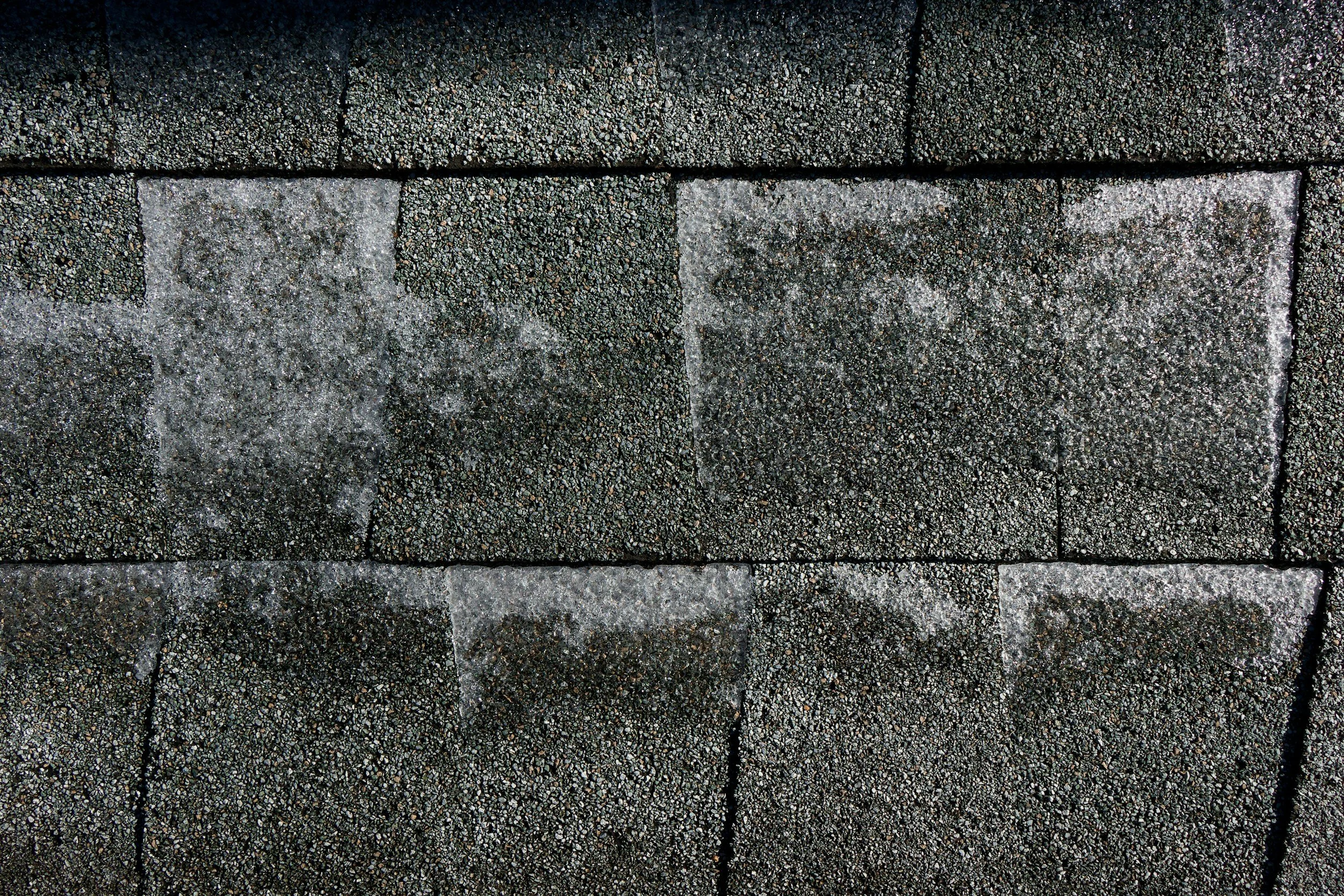 Close-up of asphalt shingles with some powdery residue on the surface.