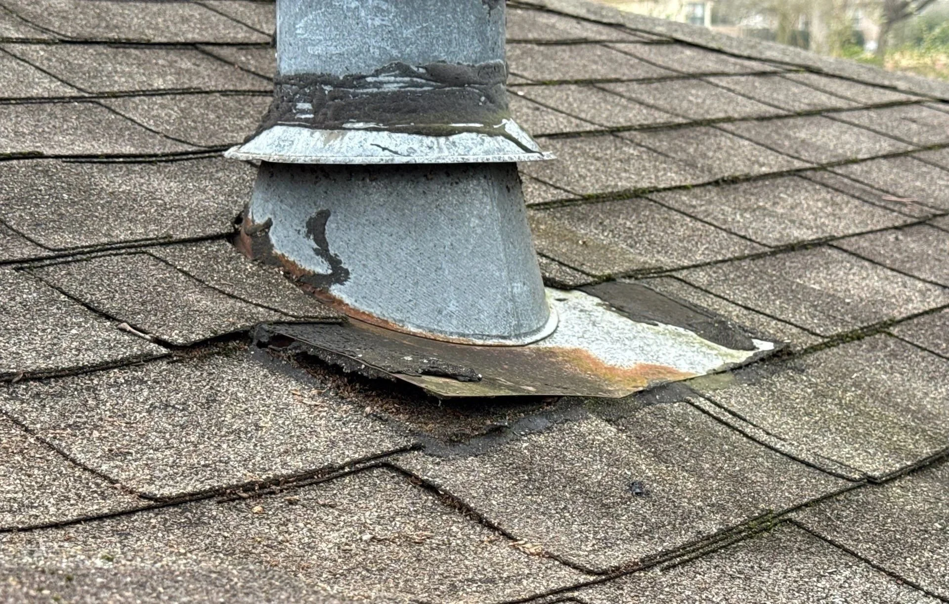 close-up photo of rusted flashing around a vent pipe on an aged asphalt shingle roof with curling shingles