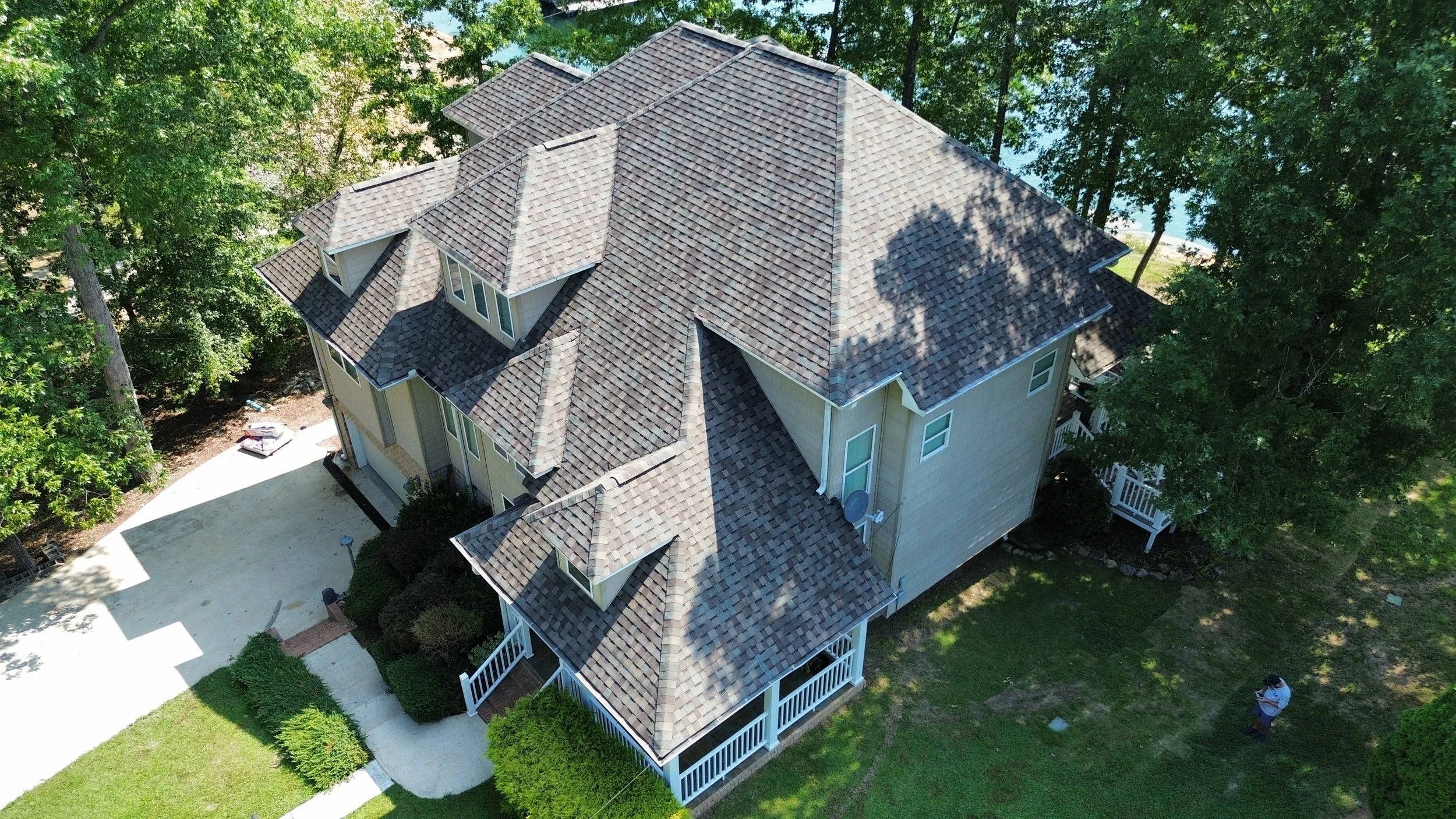 Aerial view of a suburban home with a new architectural asphalt shingle roof on a sunny day surrounded by green trees
