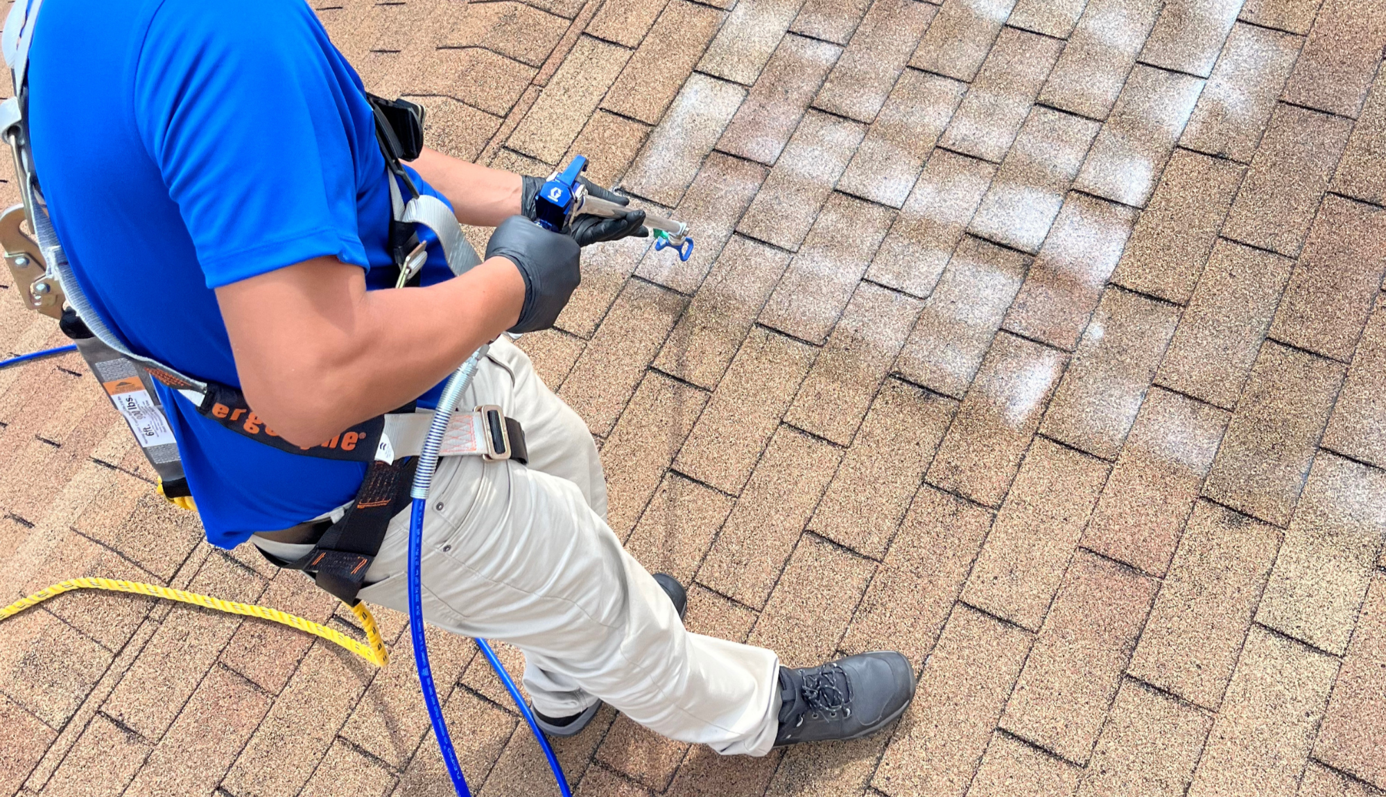 NANOROOF Technician wearing a blue shirt, khaki jeans, black shoes, and black gloves applying nanomaterial spray roof preservation treatment to asphalt shingle roof