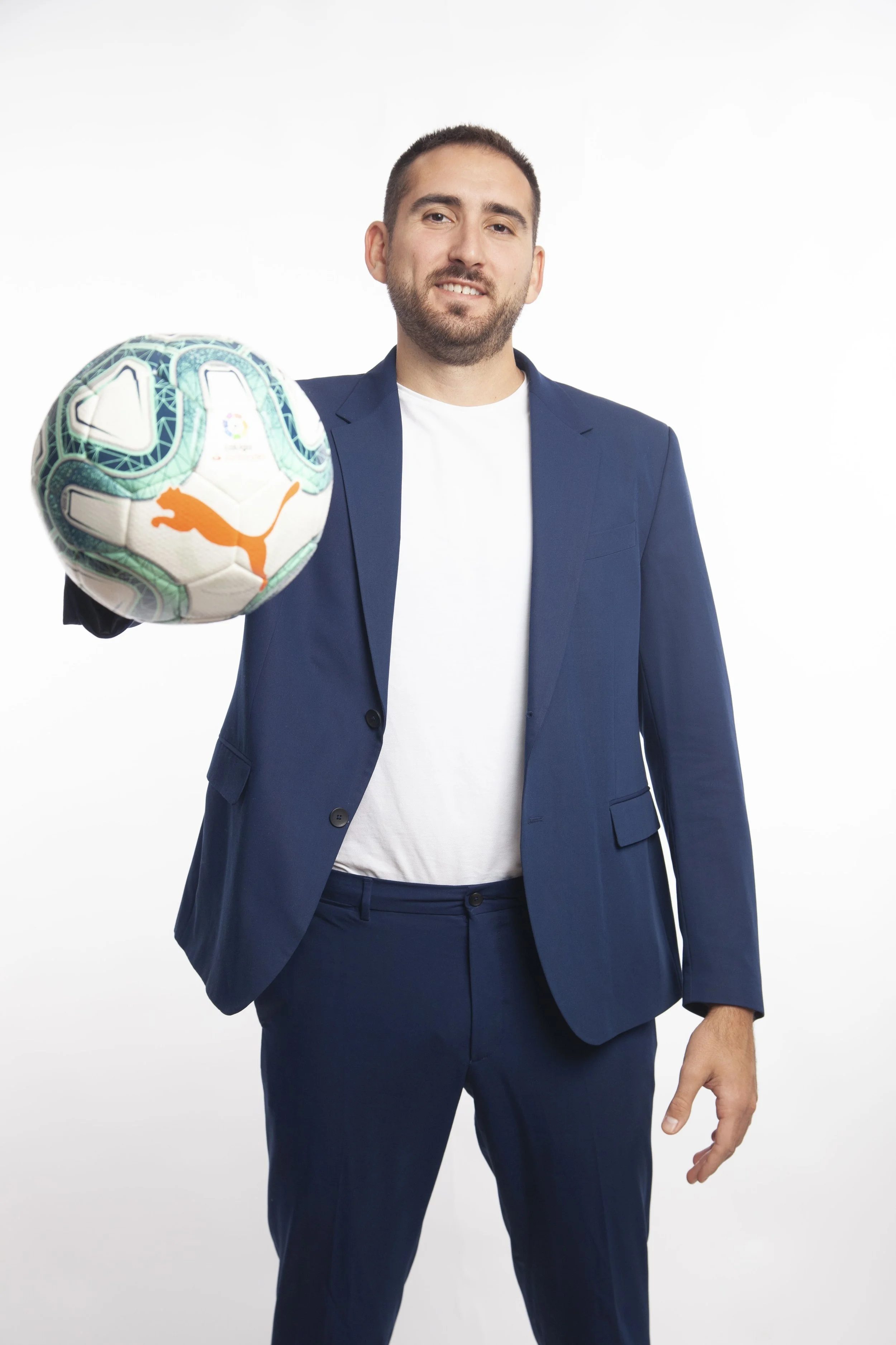 Man in blue suit holding soccer ball in white studio background.