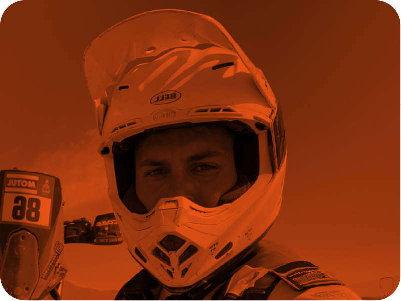 Un pilote de course portant un casque intégral, tenant une télécommande de contrôle d'un drone, avec un ciel orange en arrière-plan.