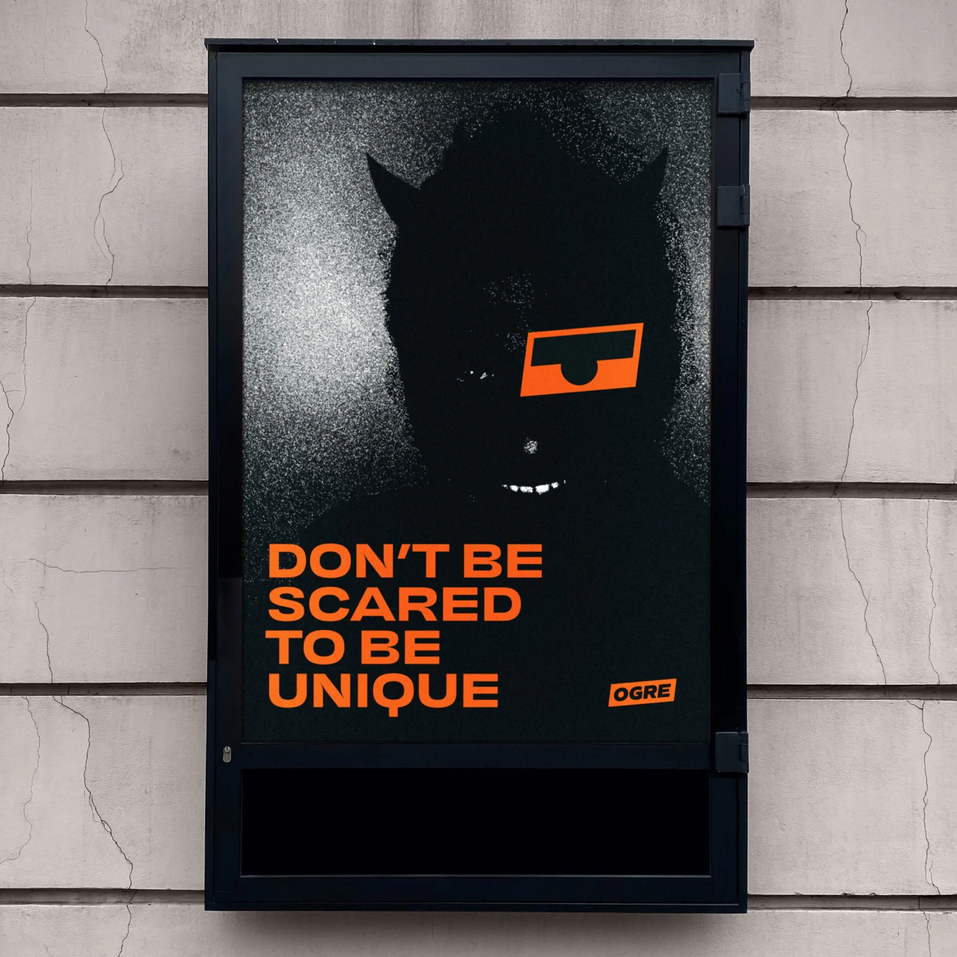 Une affiche noire avec un graphisme d'un visage de chat noir en voxel avec un œil couvert par une forme orange. Texte en orange: "DON'T BE SCARED TO BE UNIQUE" et une étiquette "OGRE".