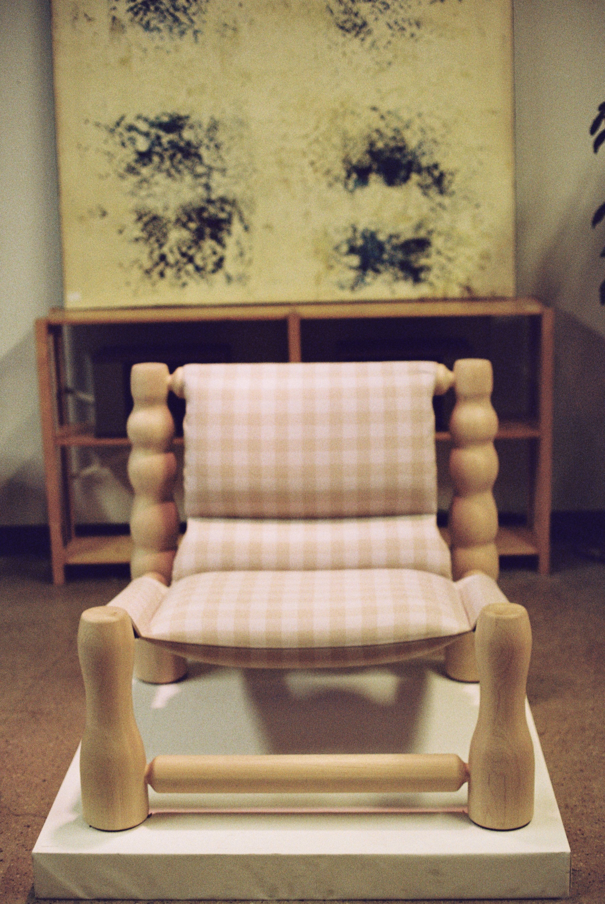 A sculptural wooden lounge chair with rounded legs and a gingham cushion, positioned in a minimalist home setting.