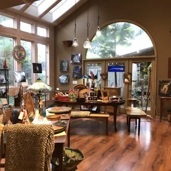 Interior of a cozy store with wooden floors, display tables, and hanging pendant lights near large windows and glass doors.