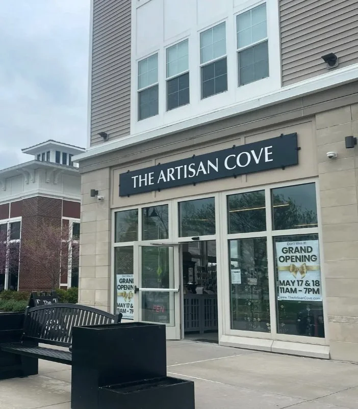 Storefront with a sign reading 'The Artisan Cove' and announcements for a grand opening on May 17 and 18 from 11 AM to 7 PM.