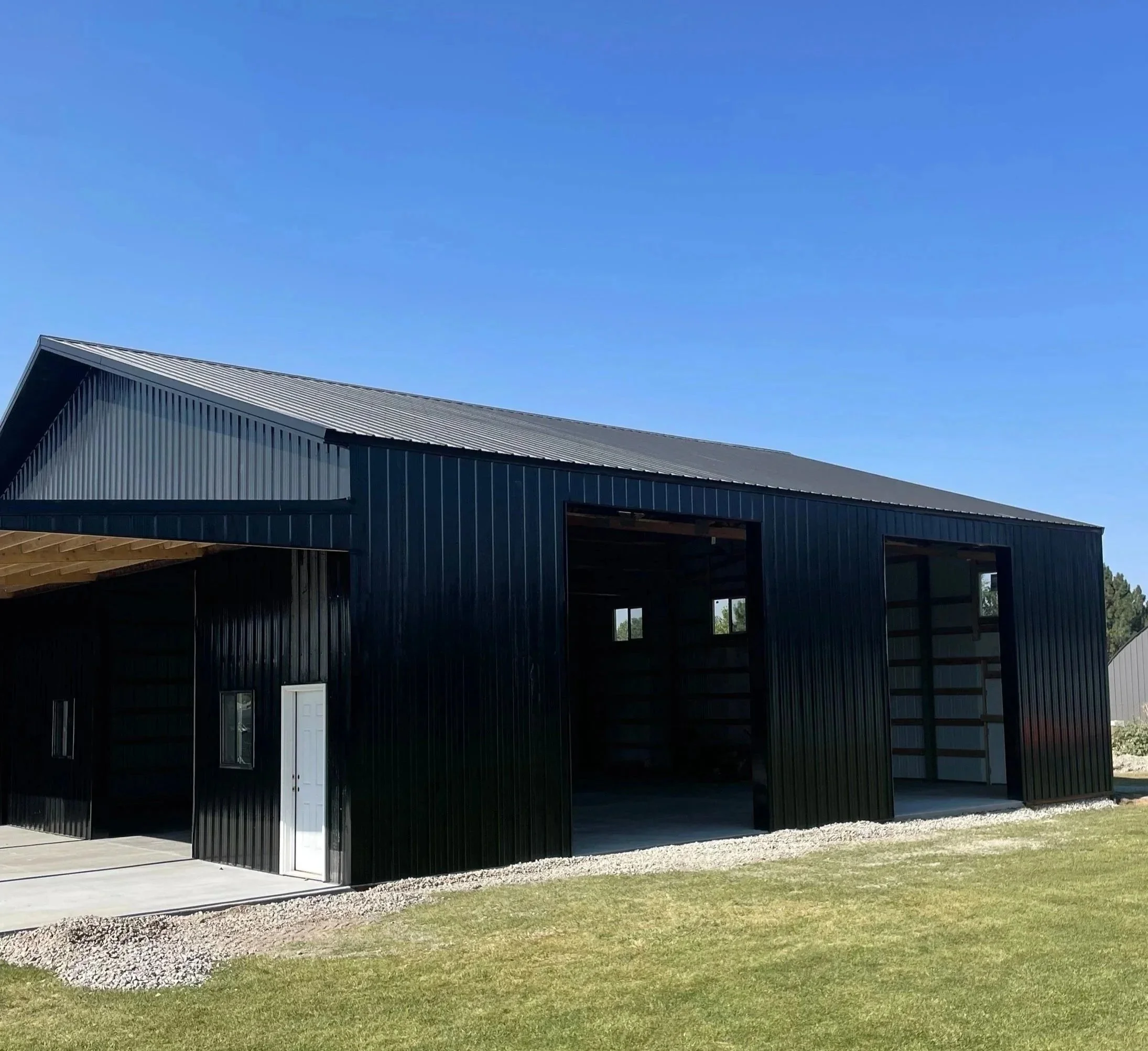 Custom black metal pole barn with multiple garage doors and concrete apron built by Sam Tams Company in Weber County Utah