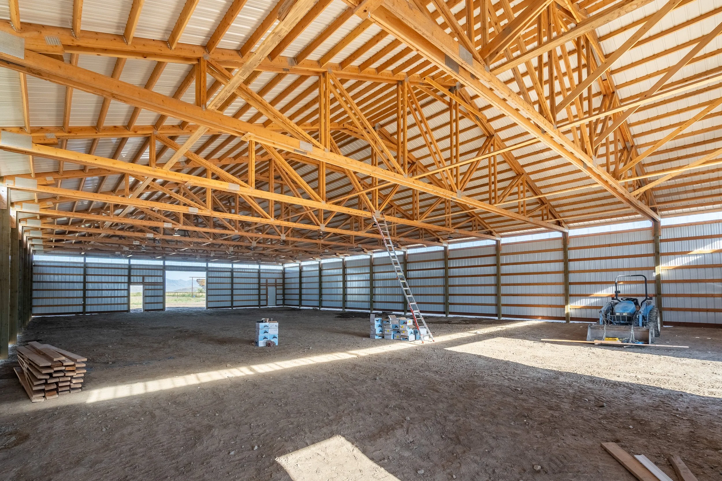 Interior of a pole barn under construction in Hooper Utah showing post frame trusses and open span design by Sam Tams Company