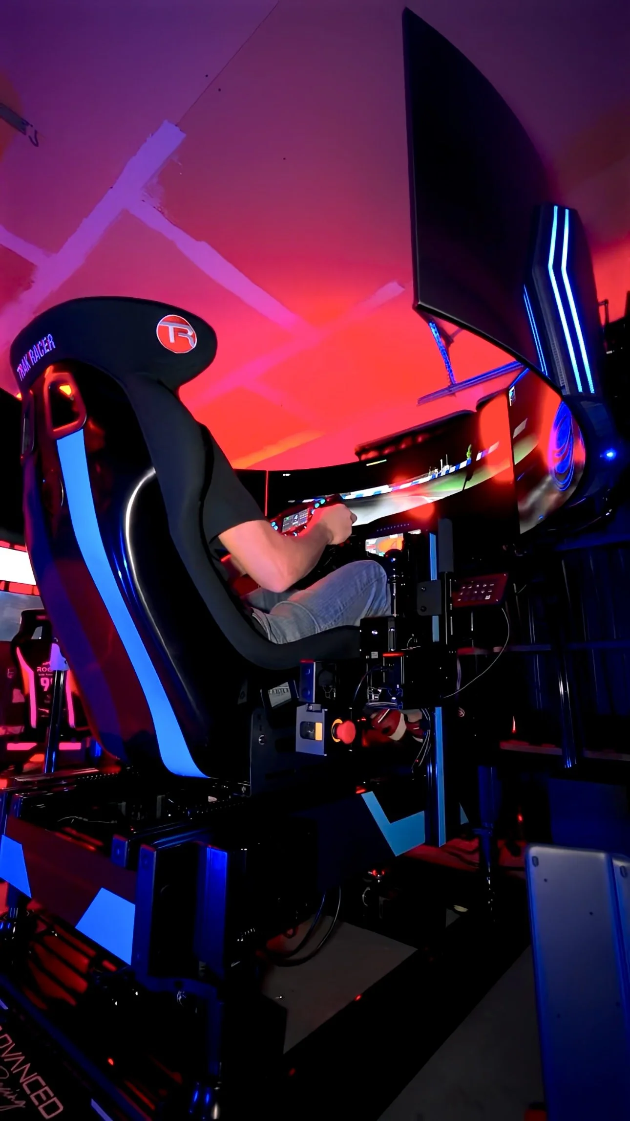 Man driving a racing simulator in a room with red and blue LED lighting