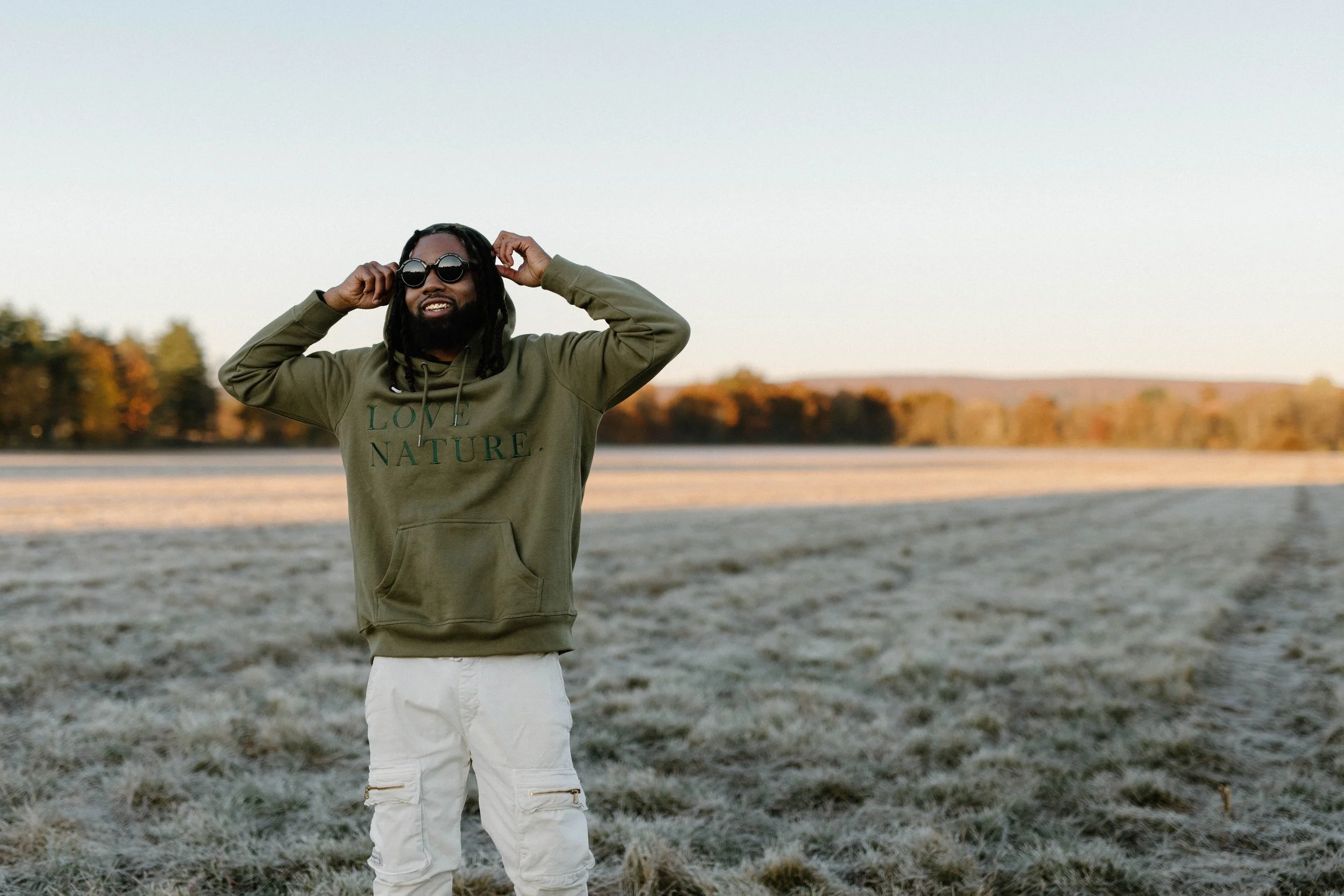 Person wearing a green "Love Nature" hoodie and sunglasses standing in a frosty field with trees in the background.
