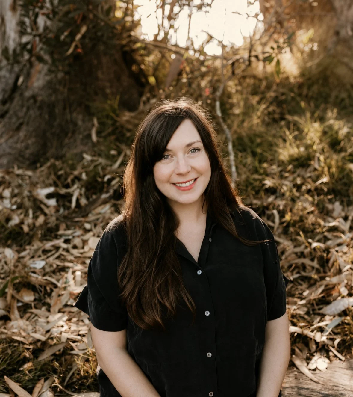 Portrait of Jess Garman, LMFT, anxiety and trauma therapist, smiling outdoors at golden hour with trees and fallen leaves in the background
