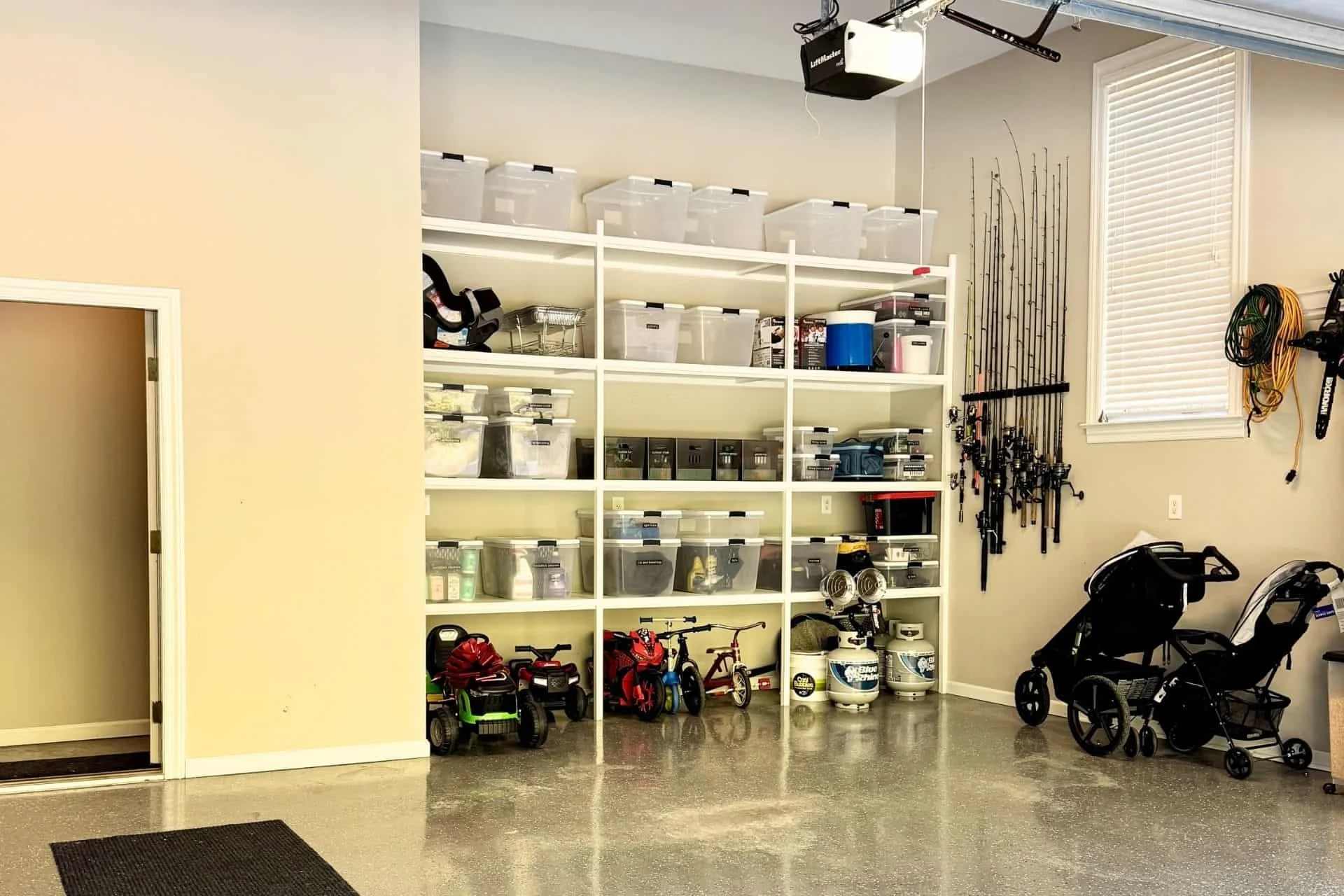 Organized garage space with shelving with bins, fishing poles on the walls and a baby stroller