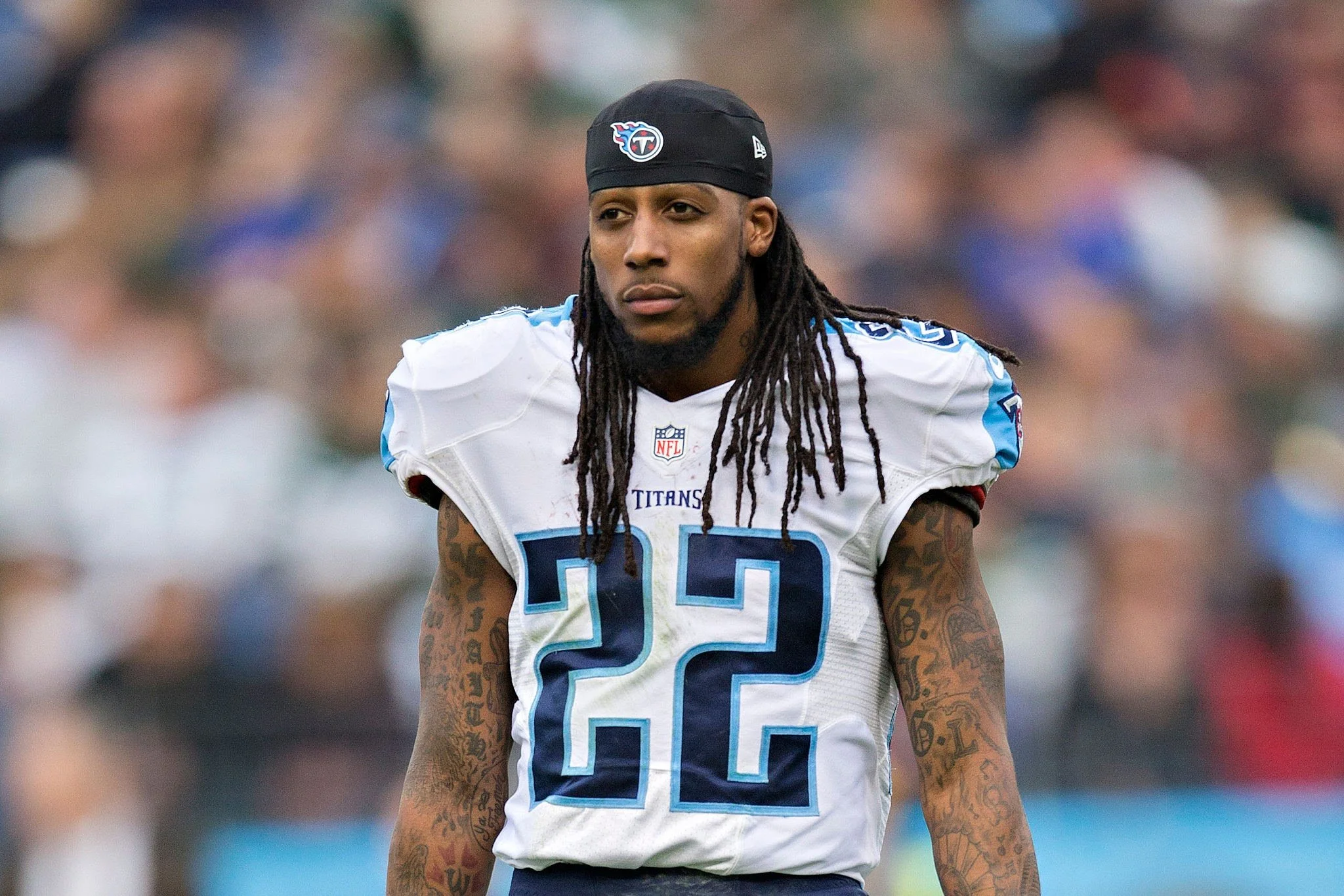 An NFL football player wearing a white Tennessee Titans jersey with the number 22, a black cap, and sporting tattoos on his arm, standing on the field during a game.